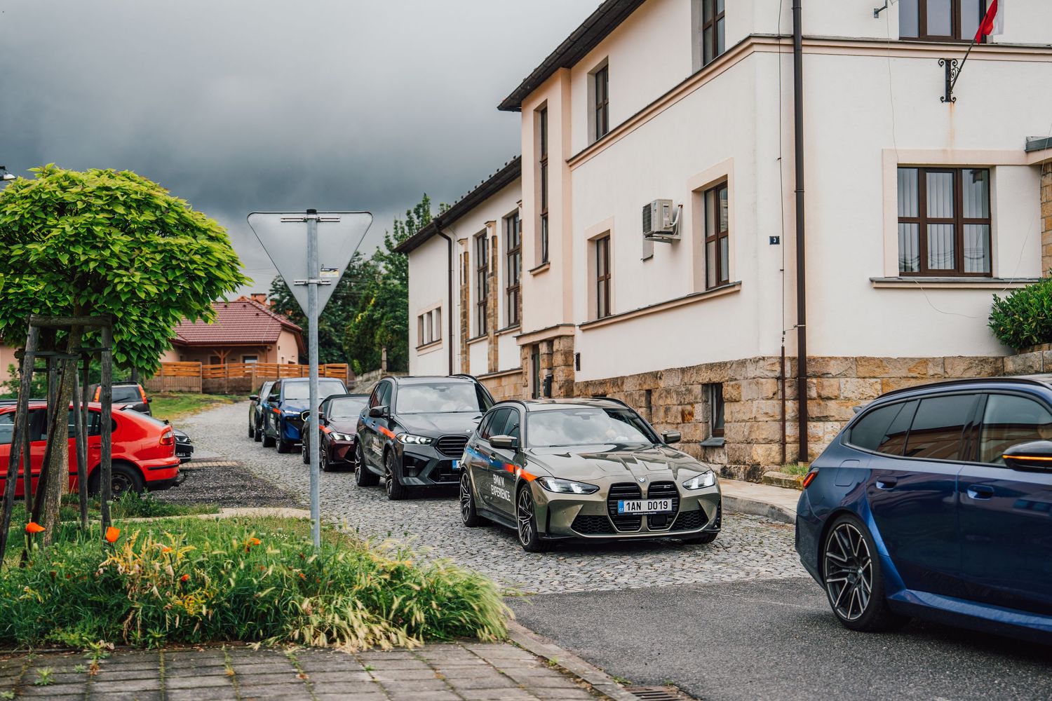 Fleet of BMW M Experience vehicles parked on cobblestone street next to a white European building.