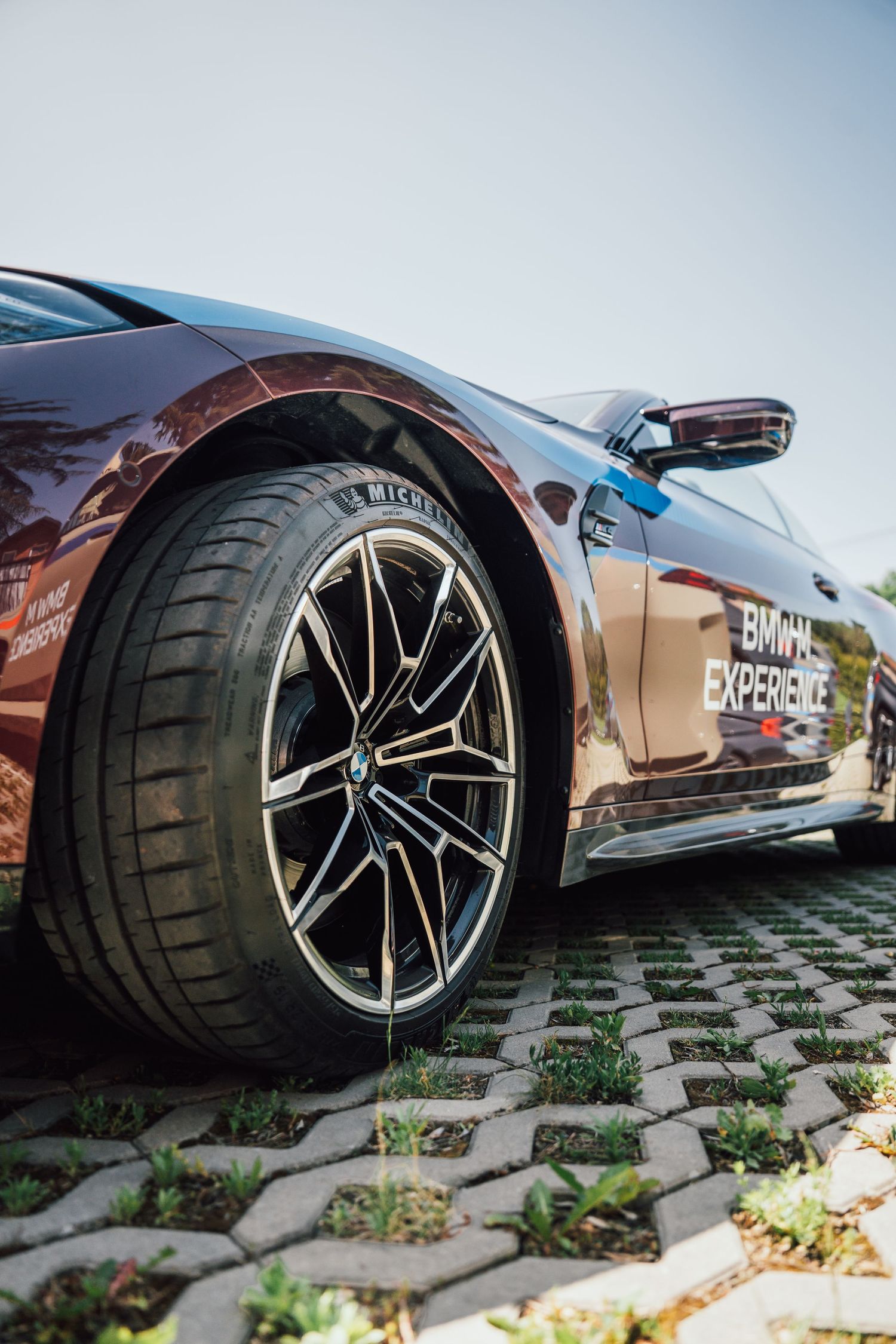 Close-up of a Michelin tire on a dark red BMW M Experience car parked on cobblestones.