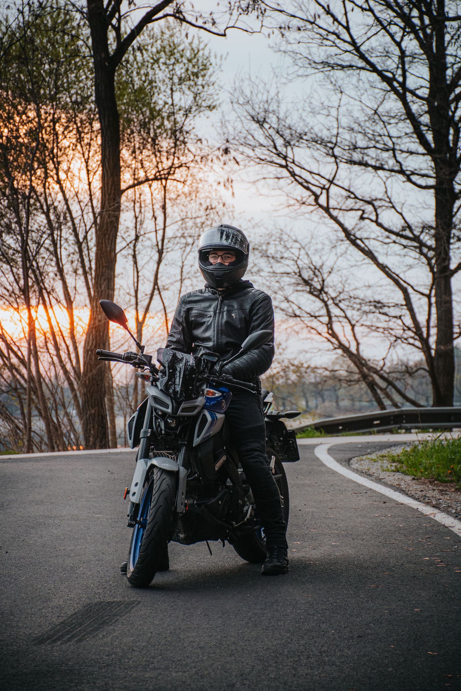 Rider in full black gear on motorcycle on winding road at dusk.
