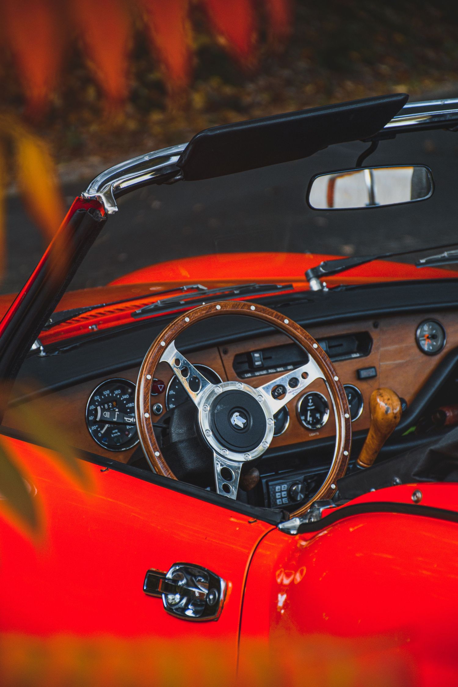 Interior view of a classic red convertible showing a wooden steering wheel and vintage dashboard.