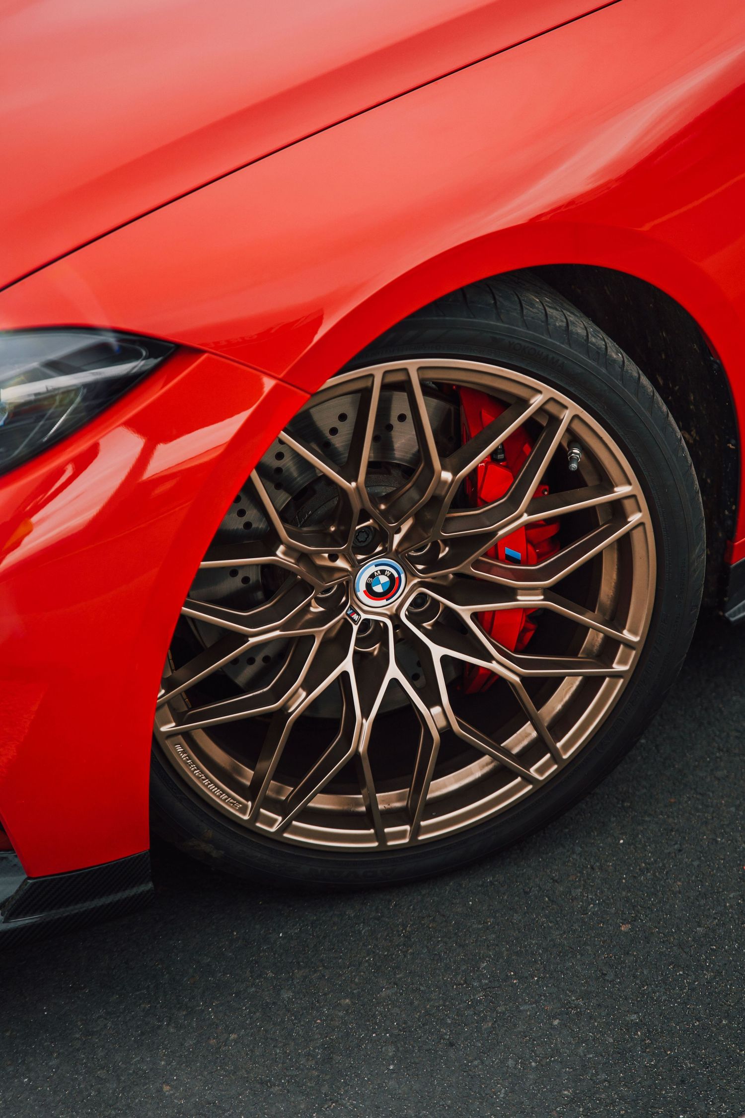 Close-up of a red BMW M4 with bronze alloy wheels and red brake calipers on a dark asphalt surface.