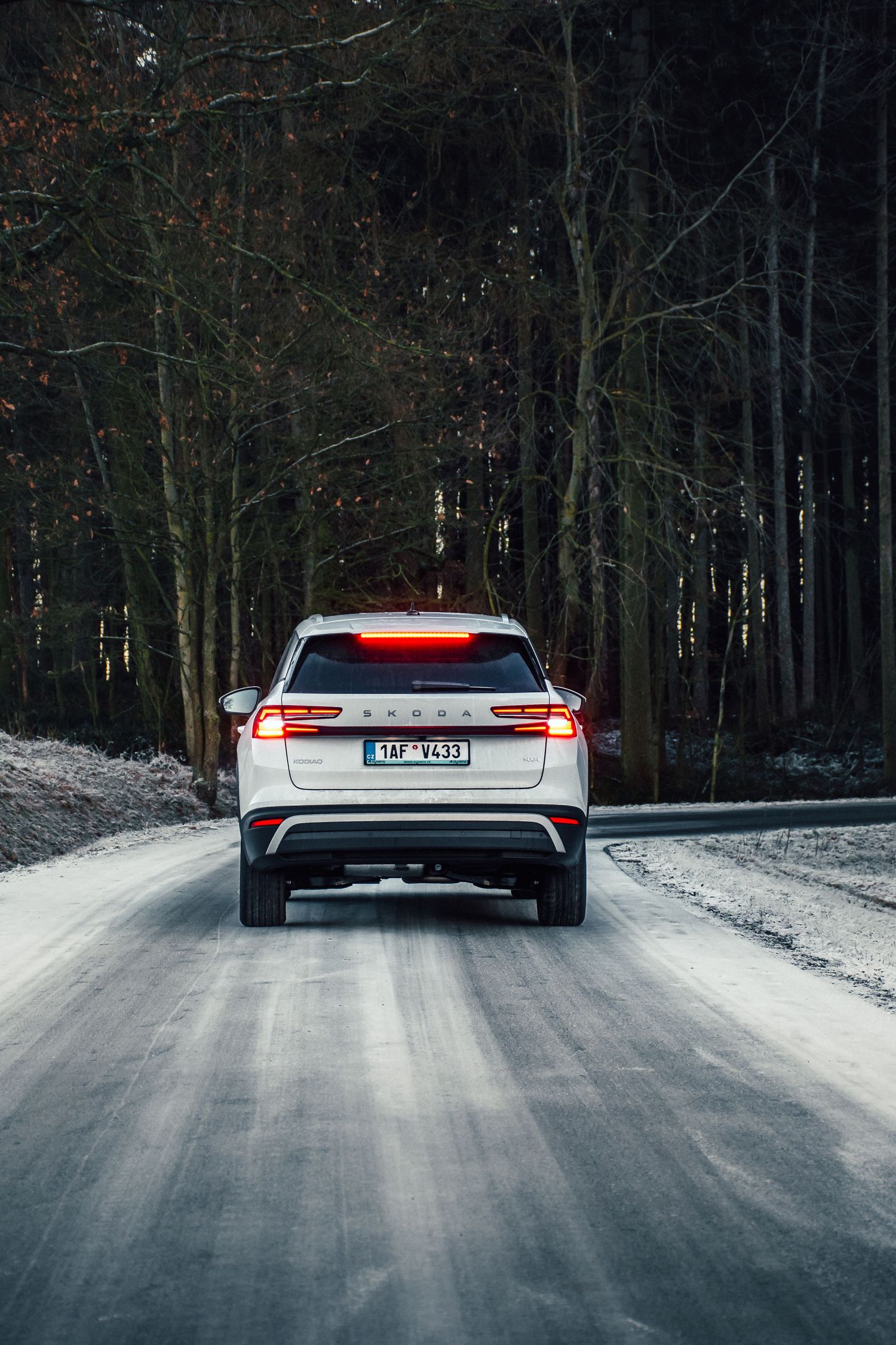 White SUV driving away on a snowy forest road with brake lights illuminated in winter conditions.