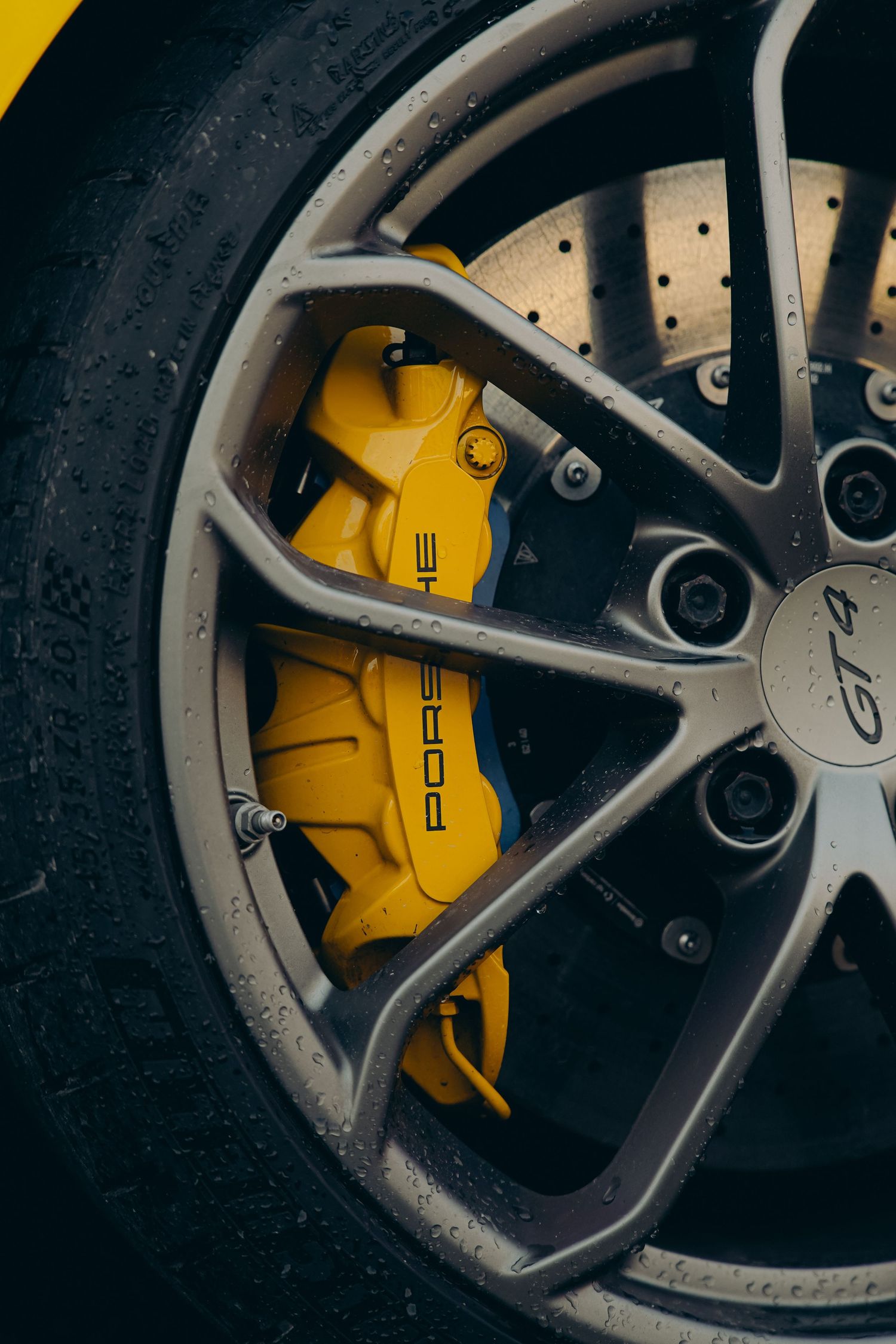 Close-up of yellow Porsche GT4 brake calipers on a silver alloy wheel with drilled rotors.