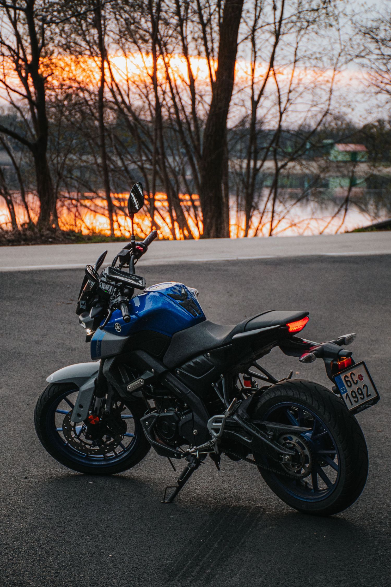 Blue Yamaha MT motorcycle parked on road at sunset near lake.