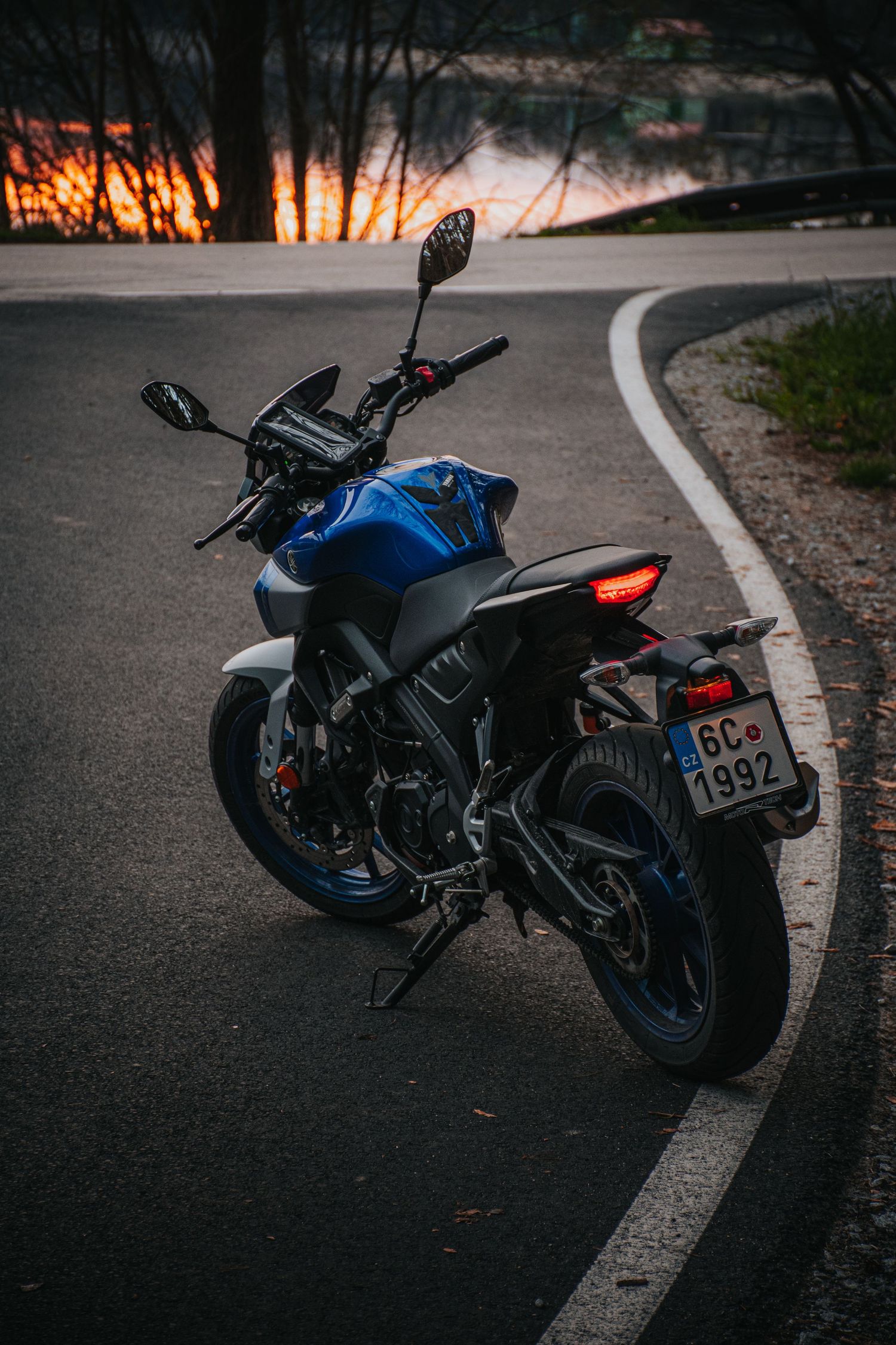 Blue Yamaha MT-07 motorcycle on curved road at golden sunset.