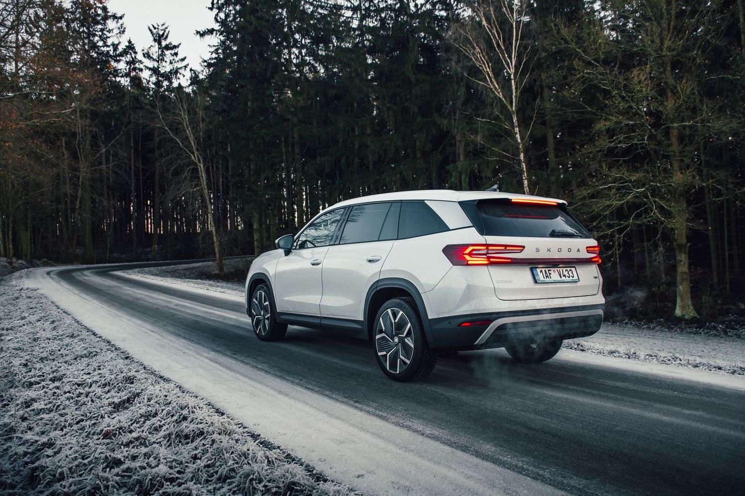 White Skoda SUV navigating a frost-covered winding road surrounded by winter forest trees.