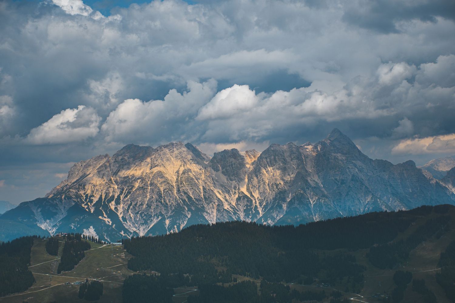 Majestic rocky mountain peaks illuminated by sunlight beneath a dramatic cloudy blue sky in the Alps.