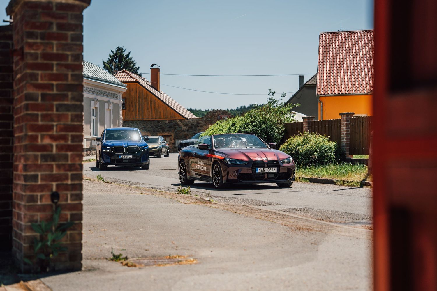 Black and red BMW sports car parked in a small village street viewed through a brick gate entrance.