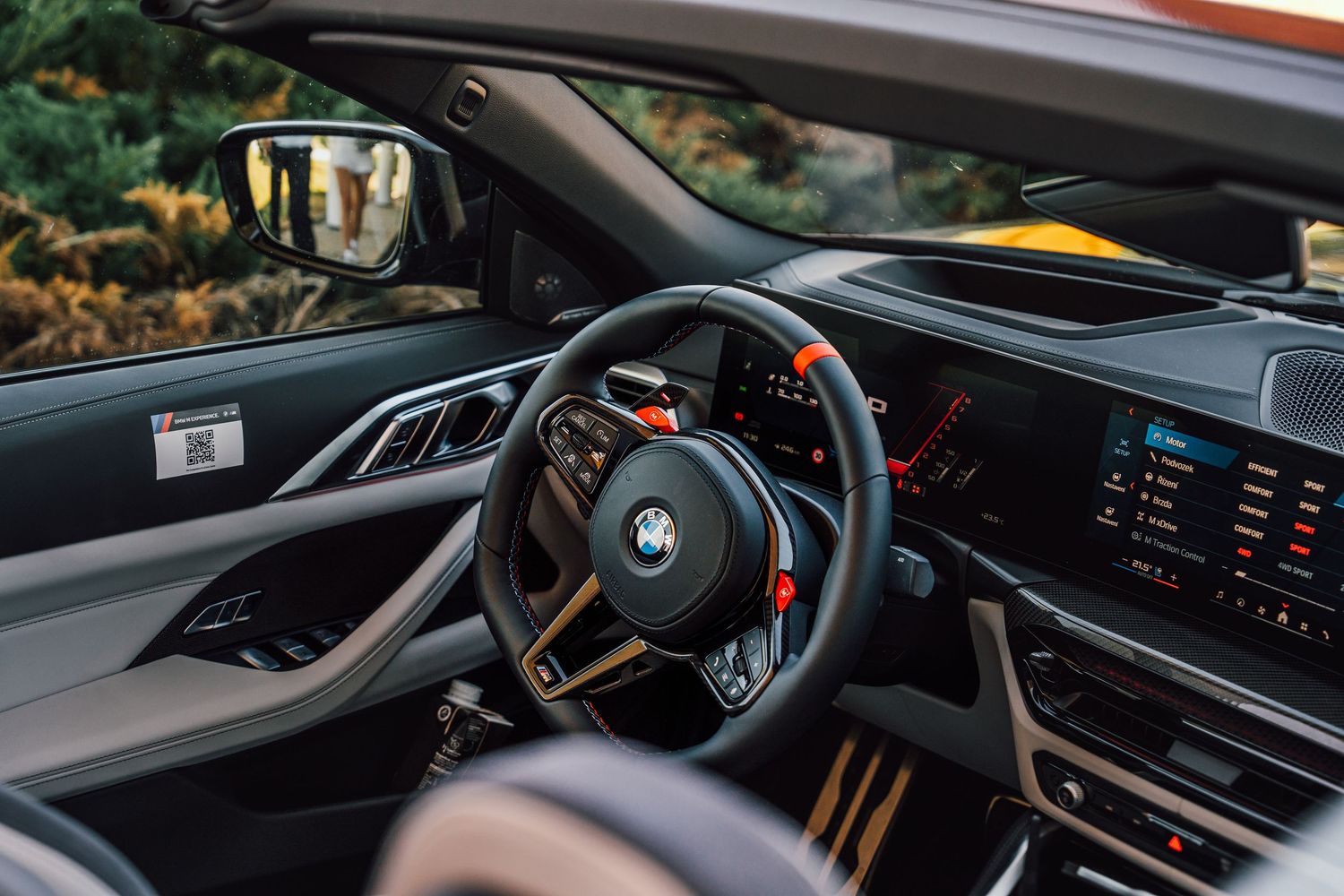BMW M car interior featuring a sport steering wheel, digital displays, and carbon fiber trim details.