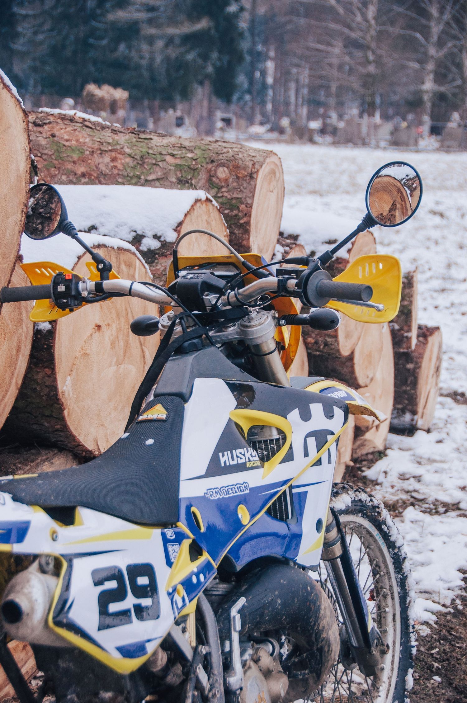 Husqvarna number 29 dirt bike parked close-up against freshly cut wooden logs in snow.