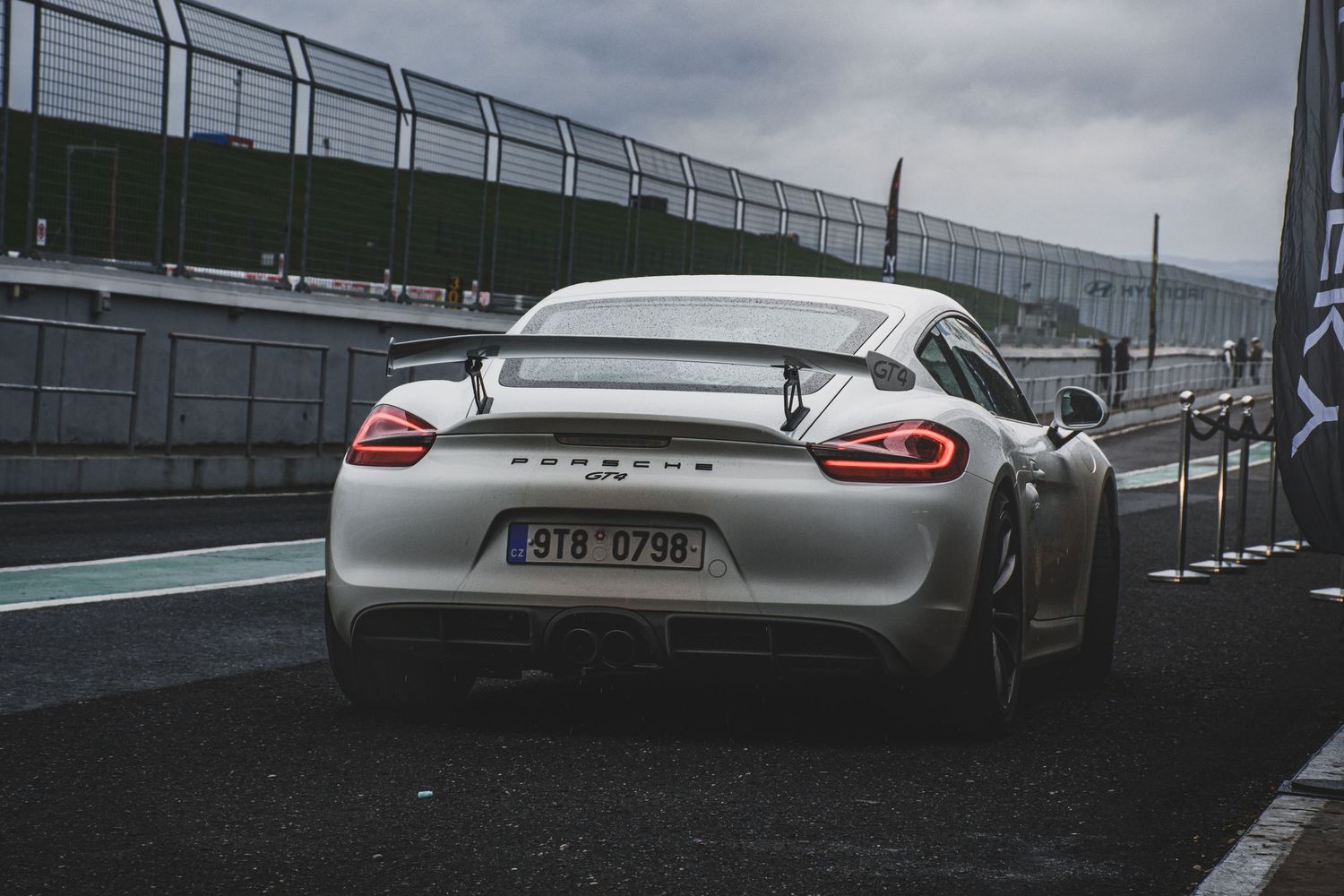 Rear view of a silver Porsche Cayman GT4 with Czech license plate on a race track.