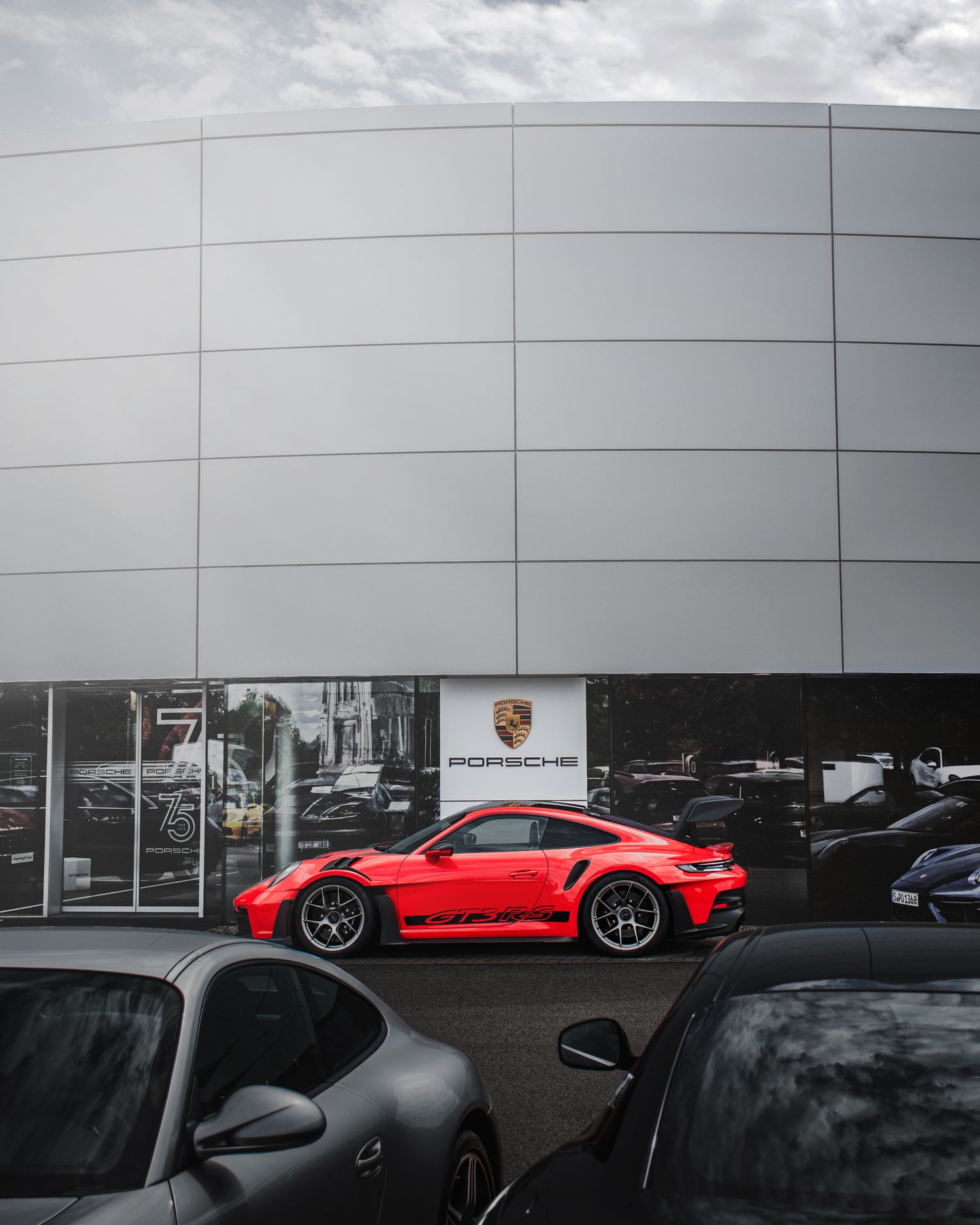 Red Porsche 911 GT3 RS displayed in a parking lot outside a Porsche dealership facade.