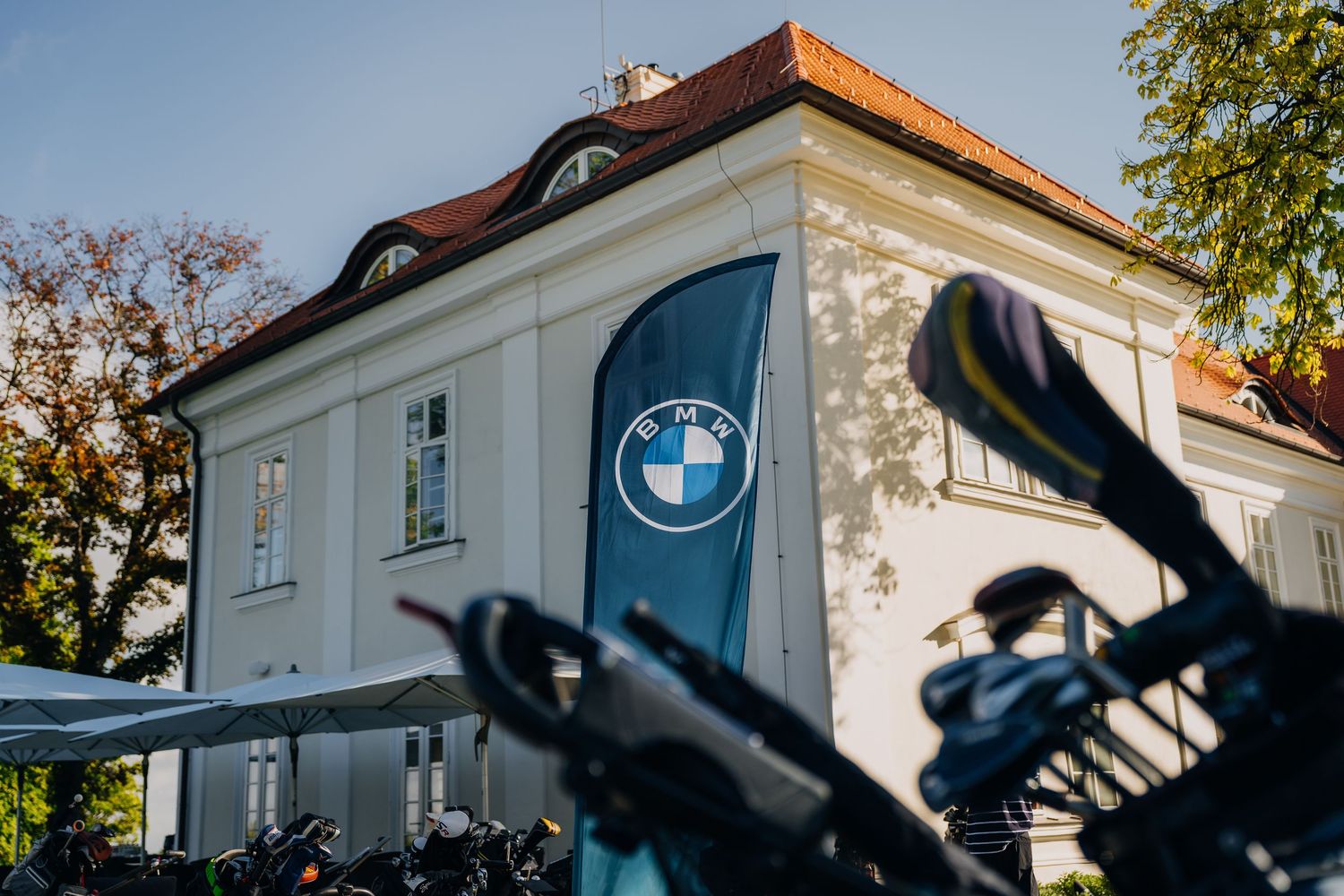 BMW branded banner on a white building facade with motorcycles parked outside at a BMW event.