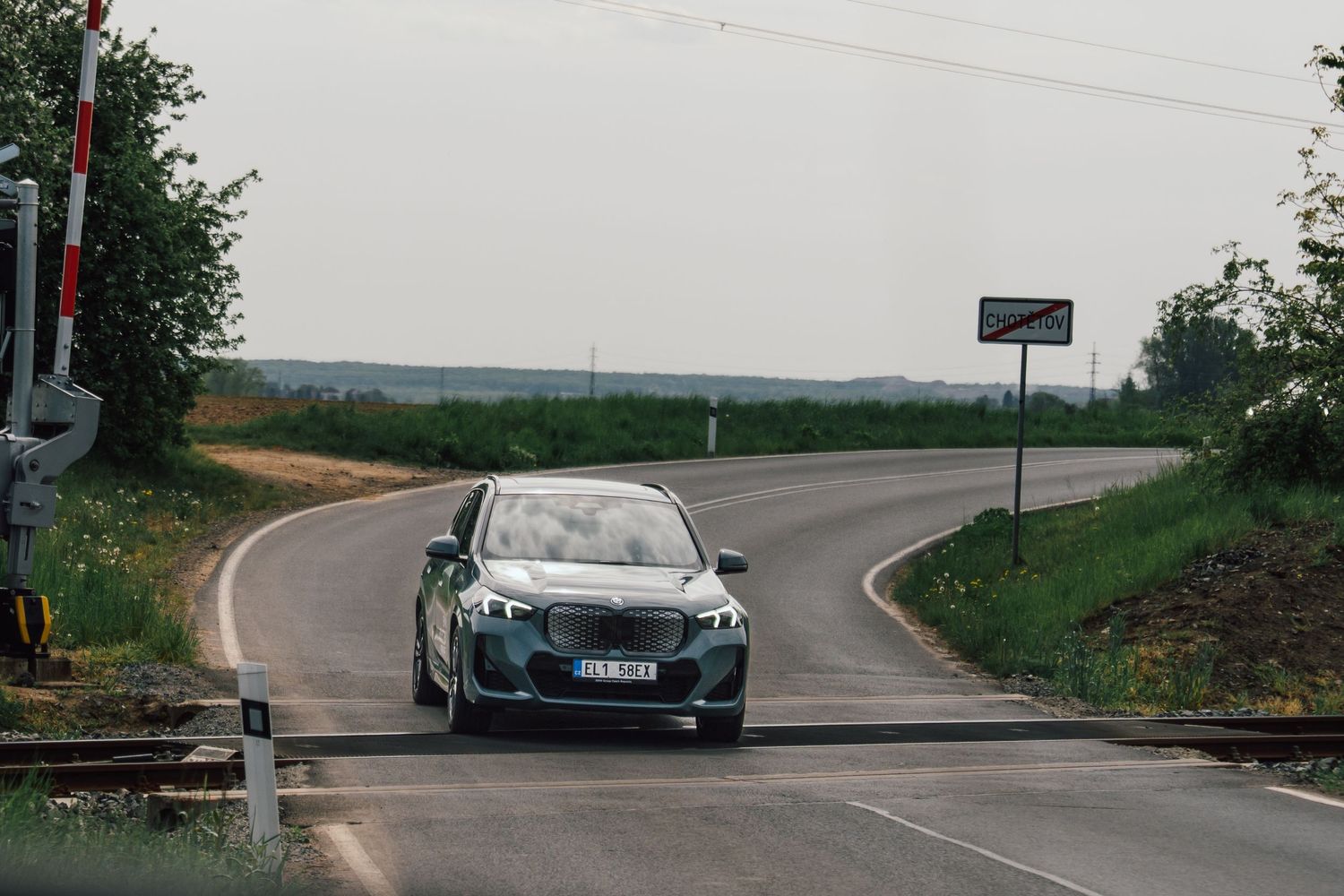 BMW electric sedan driving through a rural intersection with open fields and overcast skies in the background.