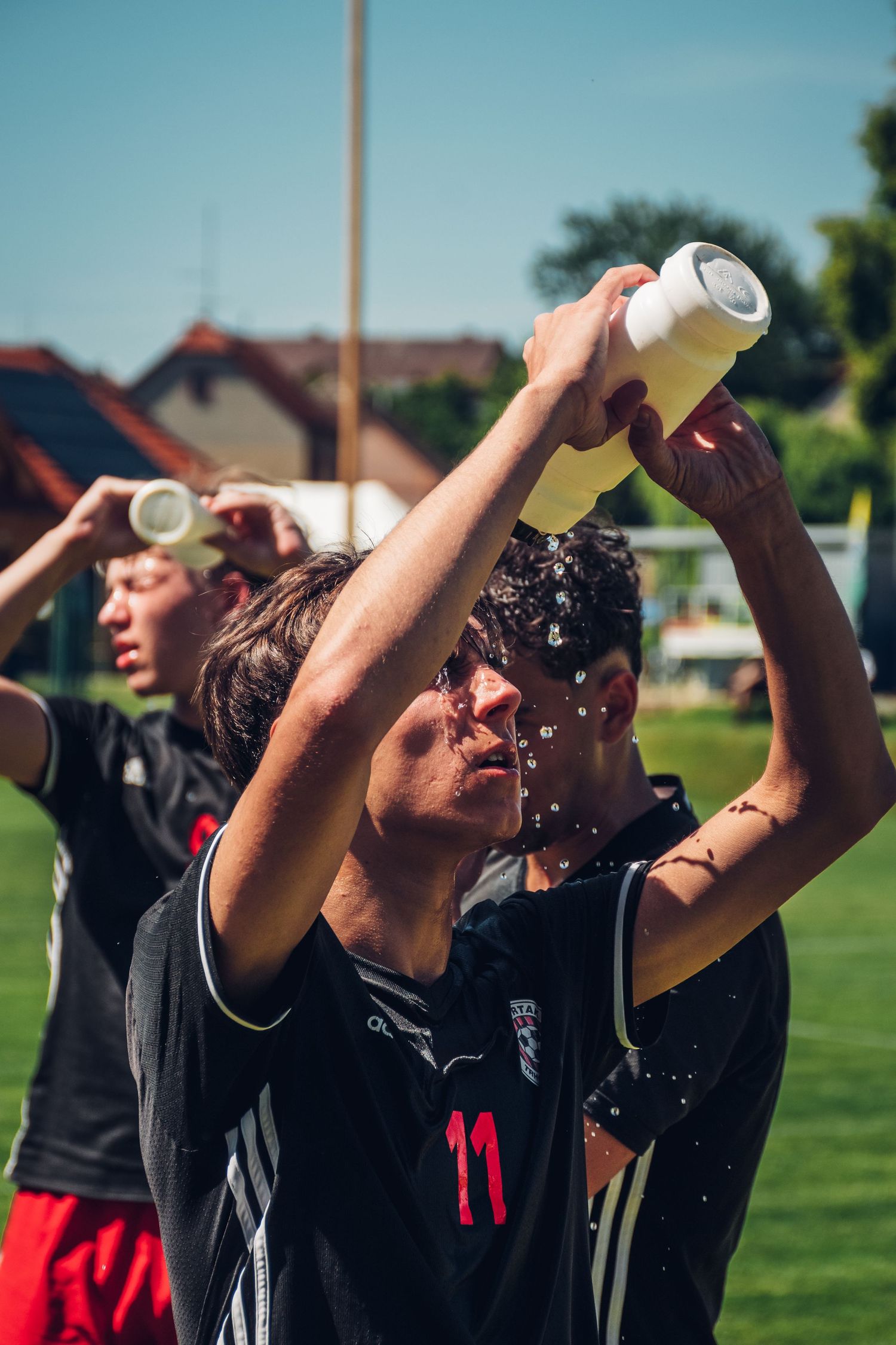 Youth soccer player in black number 11 jersey pours water over his face to cool down.