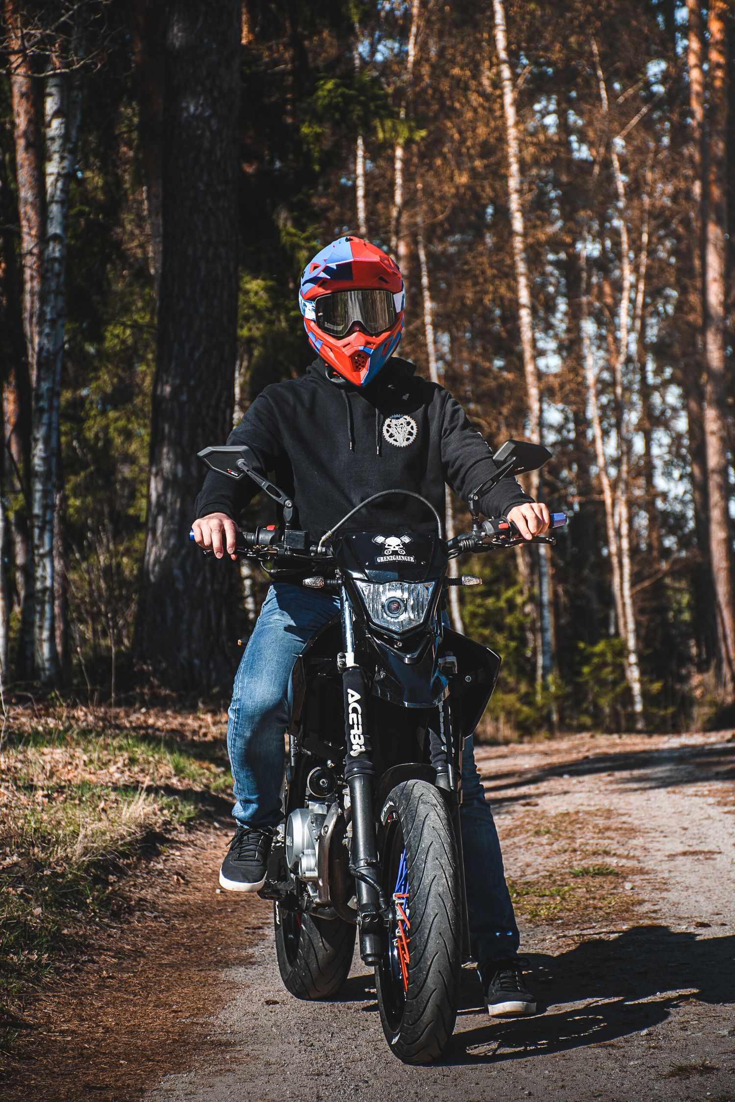 Motocross rider in red helmet on black dirt bike on forest trail.