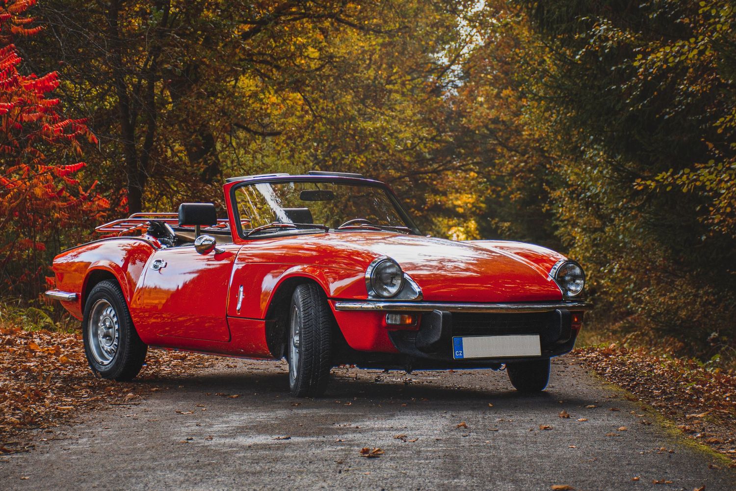 Classic red open-top sports car parked on a scenic autumn forest road.