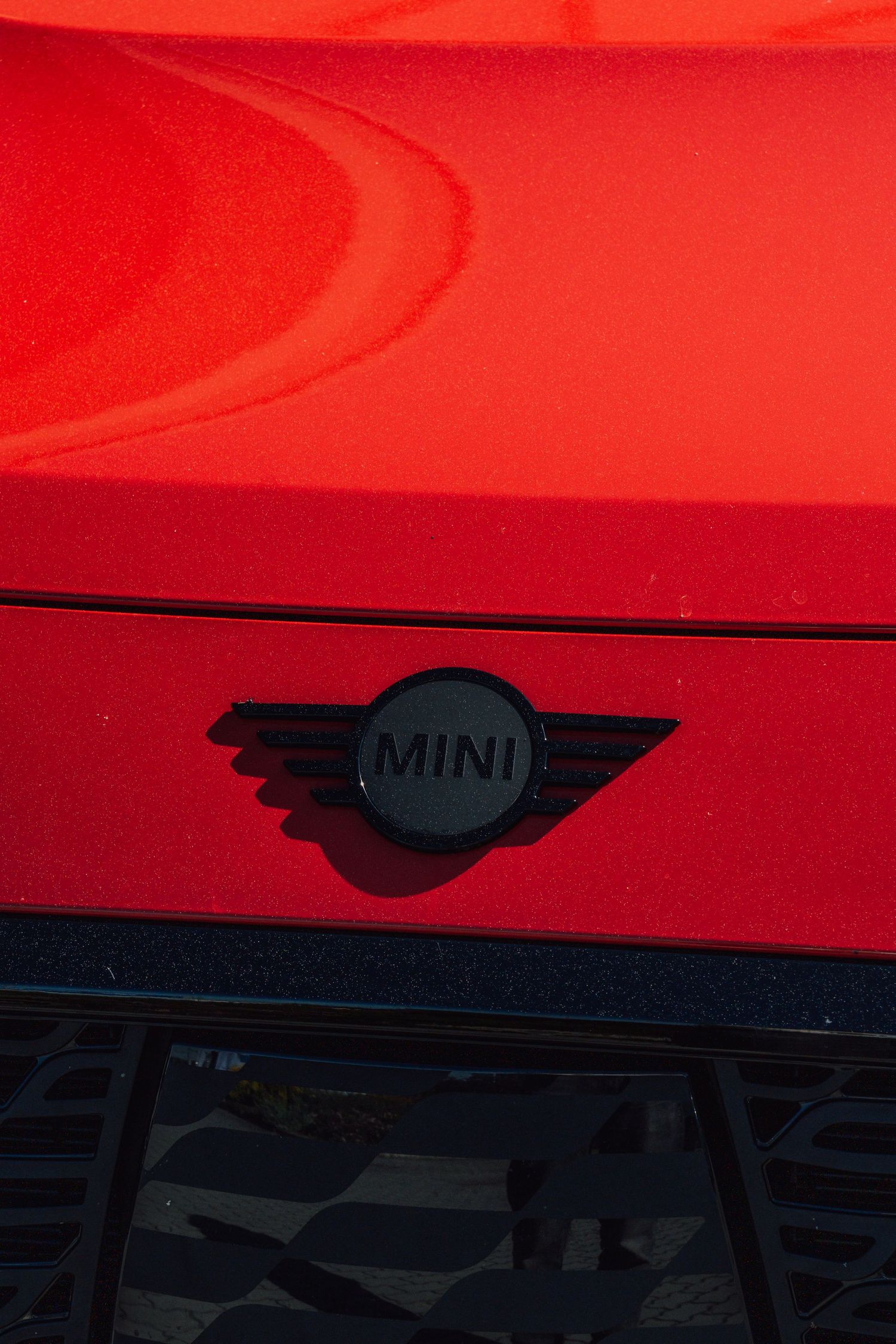 Close-up of black MINI logo badge on vibrant red car hood surface.