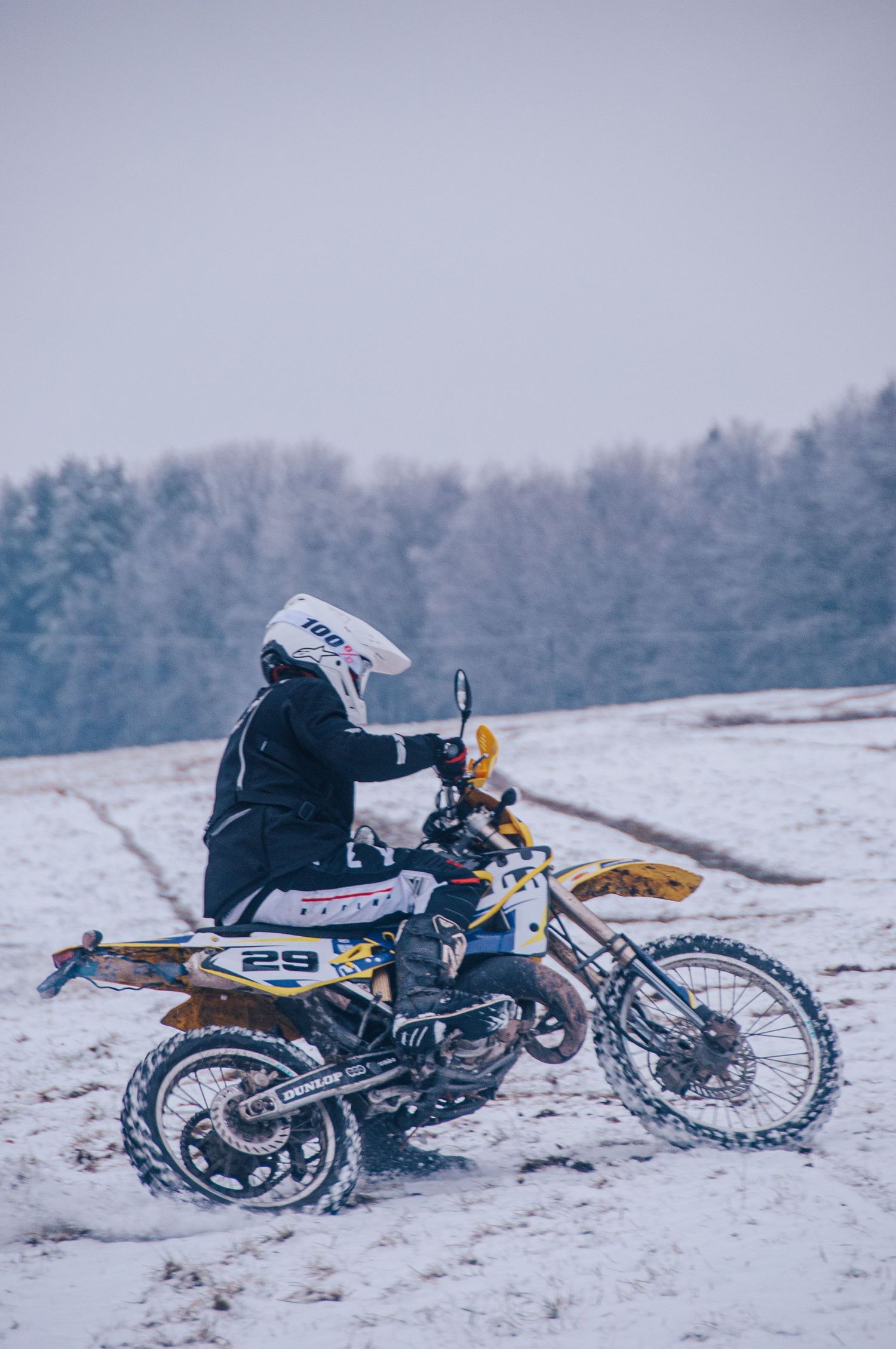 Motocross rider on a yellow dirt bike navigating a snowy field in winter conditions.