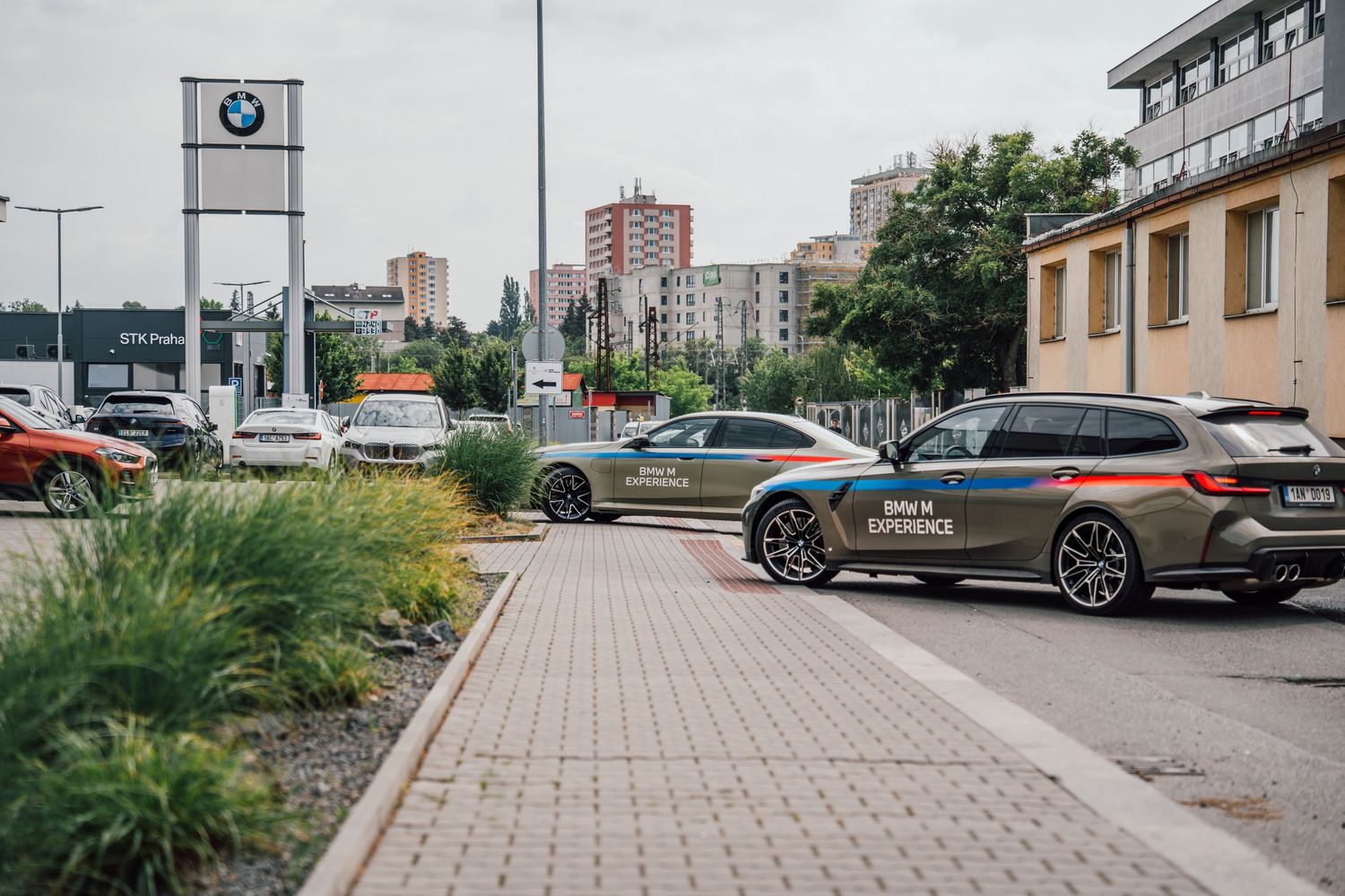 BMW dealership exterior with branded vehicles parked along a tree-lined street in an urban setting.