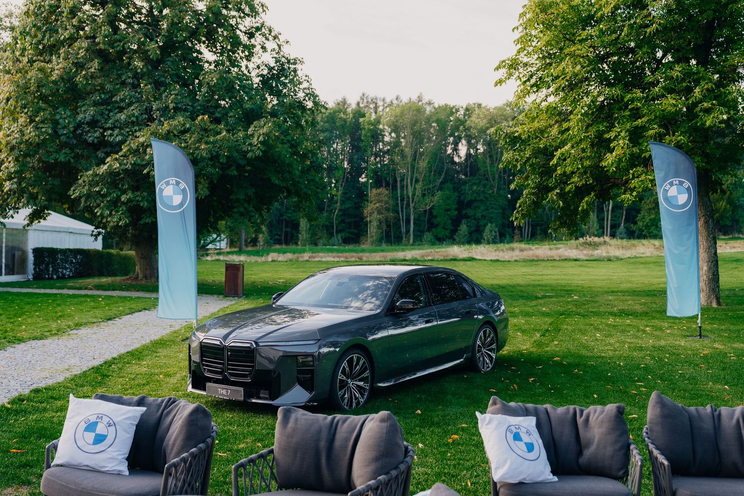 Dark green BMW sedan displayed on grass at a BMW Golf Cup event with branded flags and outdoor seating.