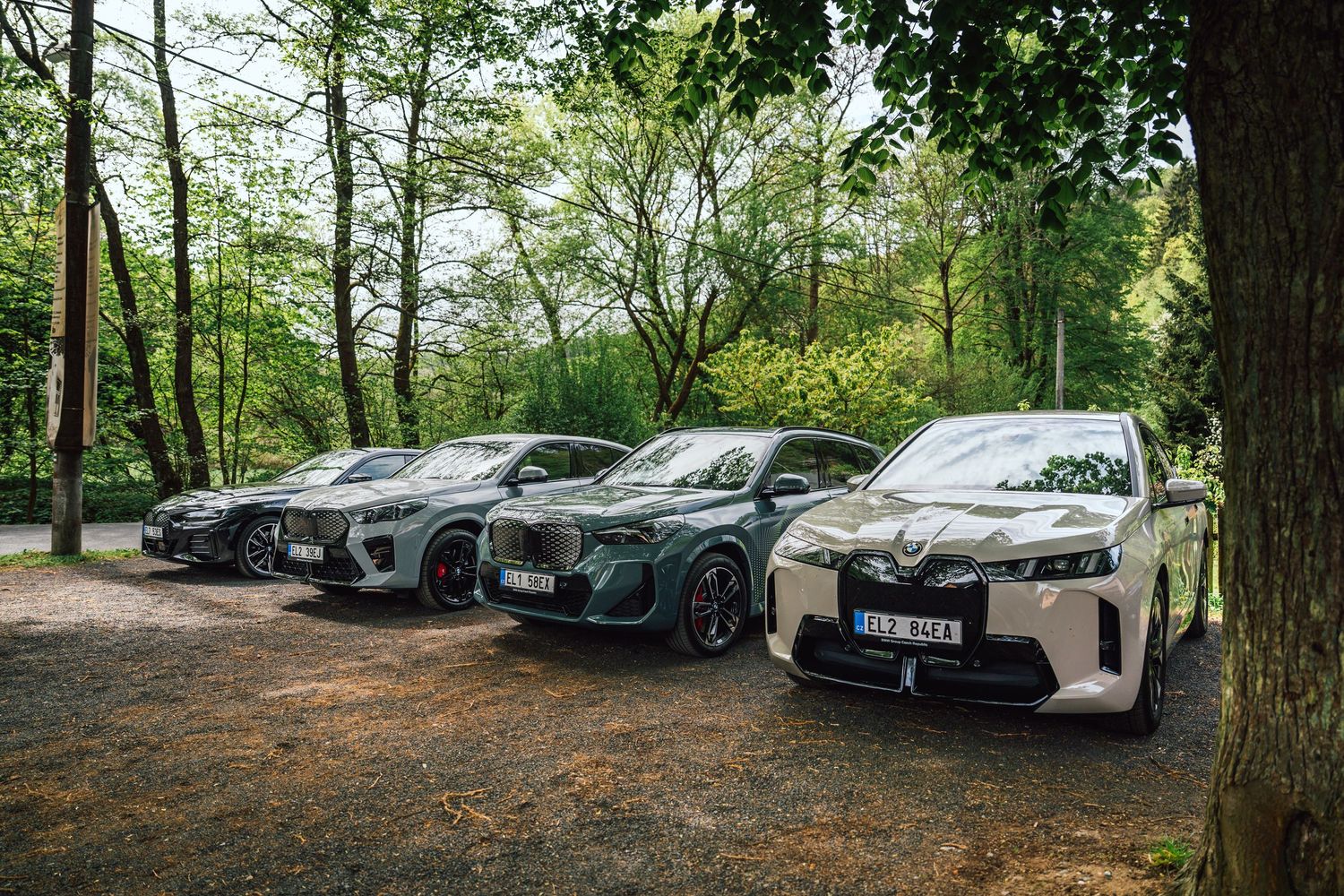 Four BMW electric SUVs lined up on a forest gravel path during an outdoor automotive showcase event.