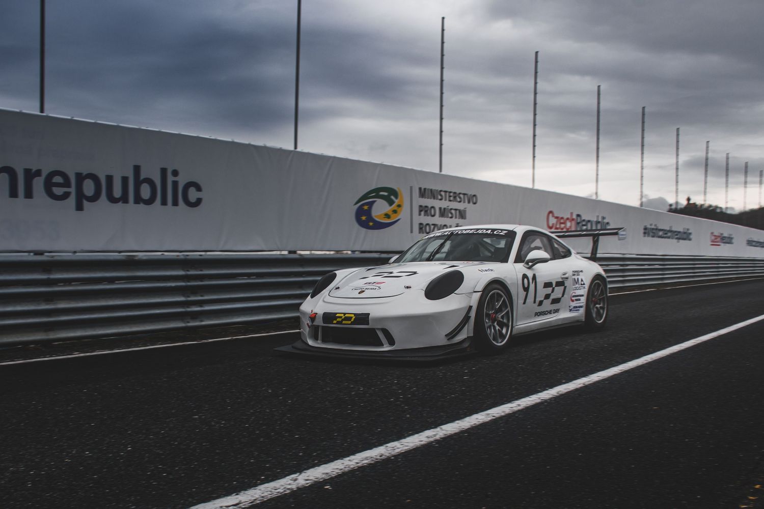 White Porsche 911 GT3 Cup race car parked on track with Visit Czech Republic wall signage.