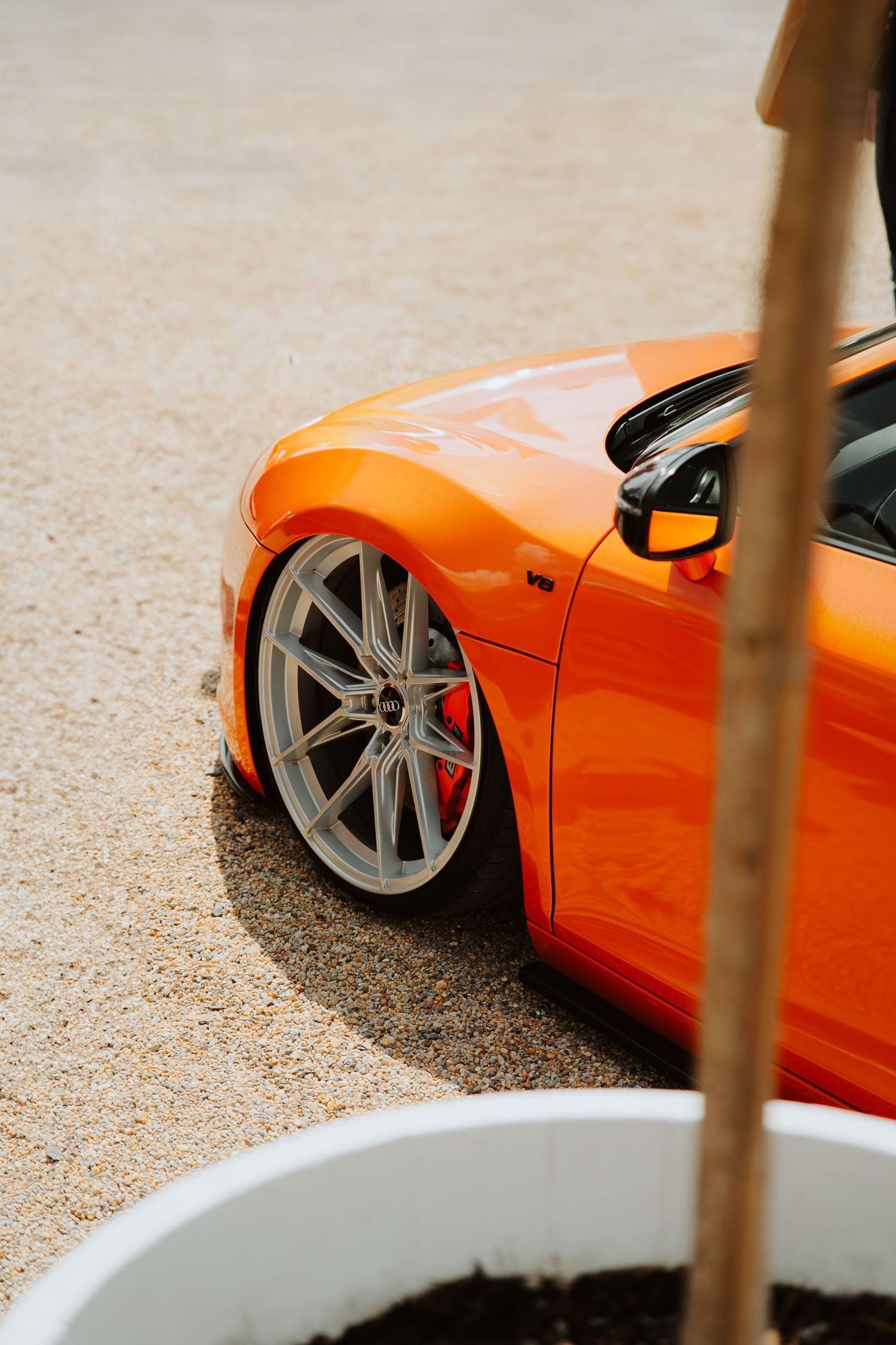 Lowered orange sports car with polished silver BBS wheels and red brake calipers on a sandy surface.