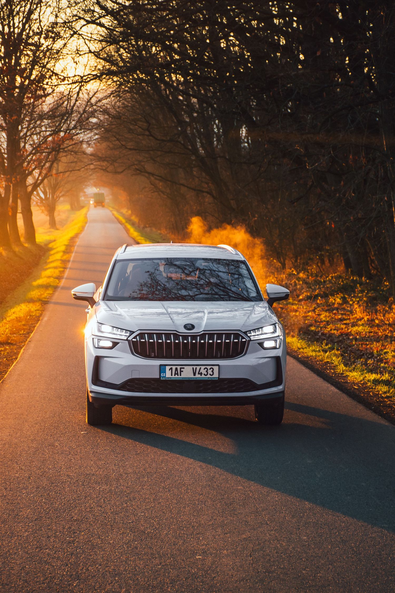 White Skoda SUV driving on a scenic road bathed in warm golden sunset light.