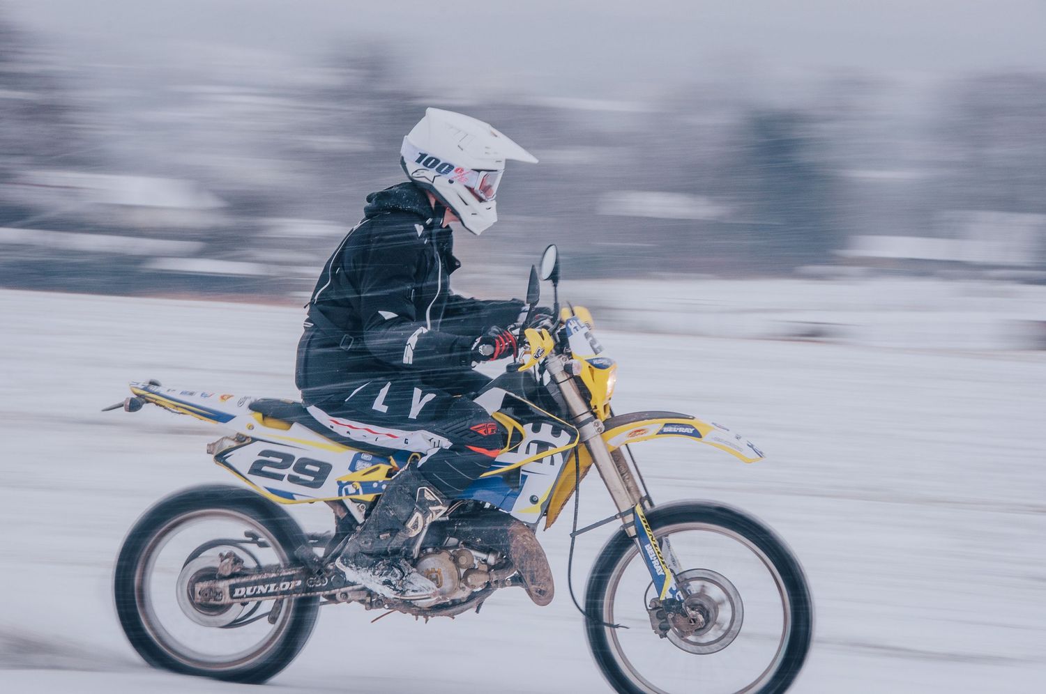 Motocross racer number 29 speeds on Husqvarna dirt bike across snowy winter terrain.