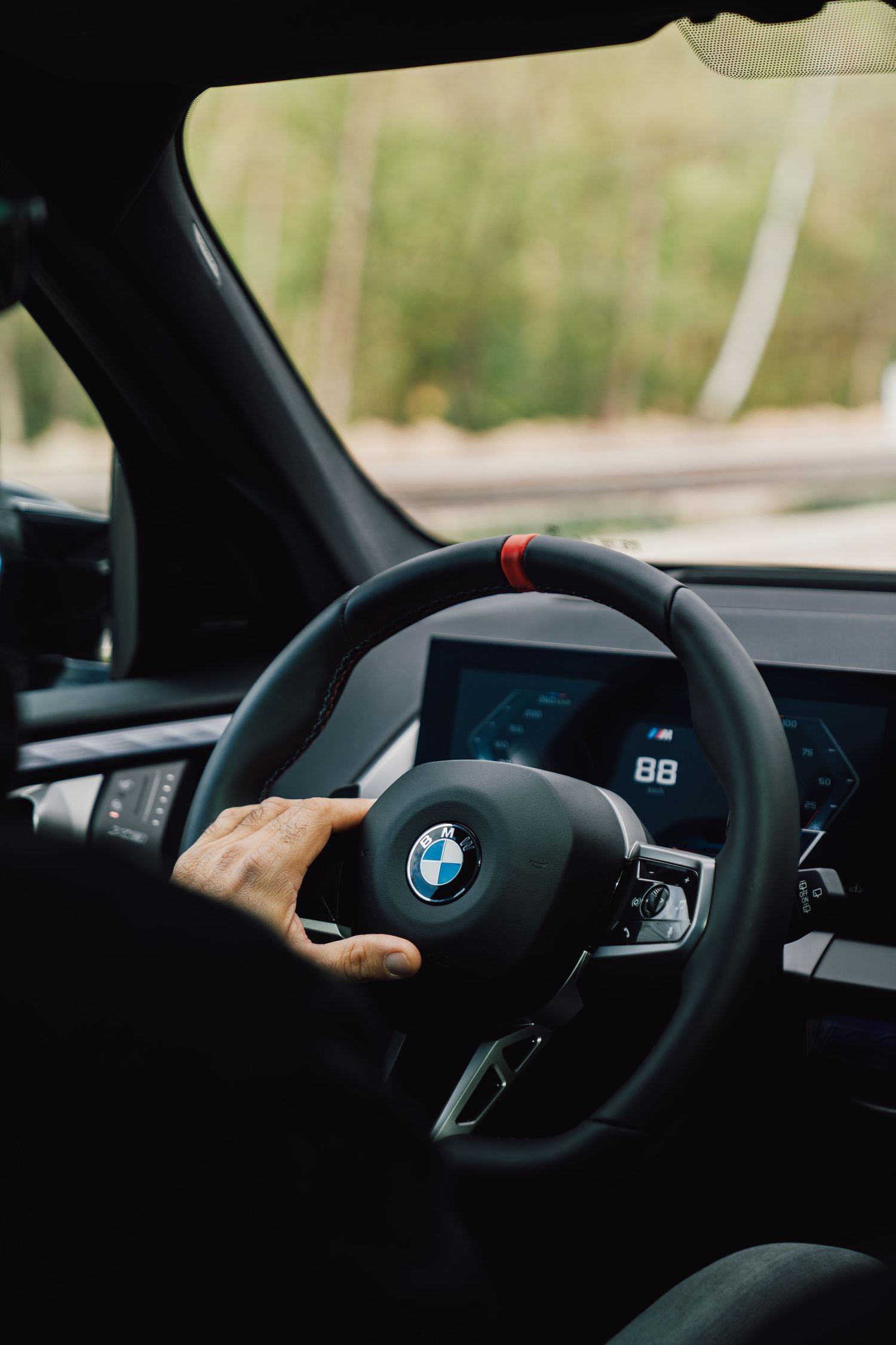 Driver gripping a BMW M steering wheel with red accent stitch inside a luxury vehicle.