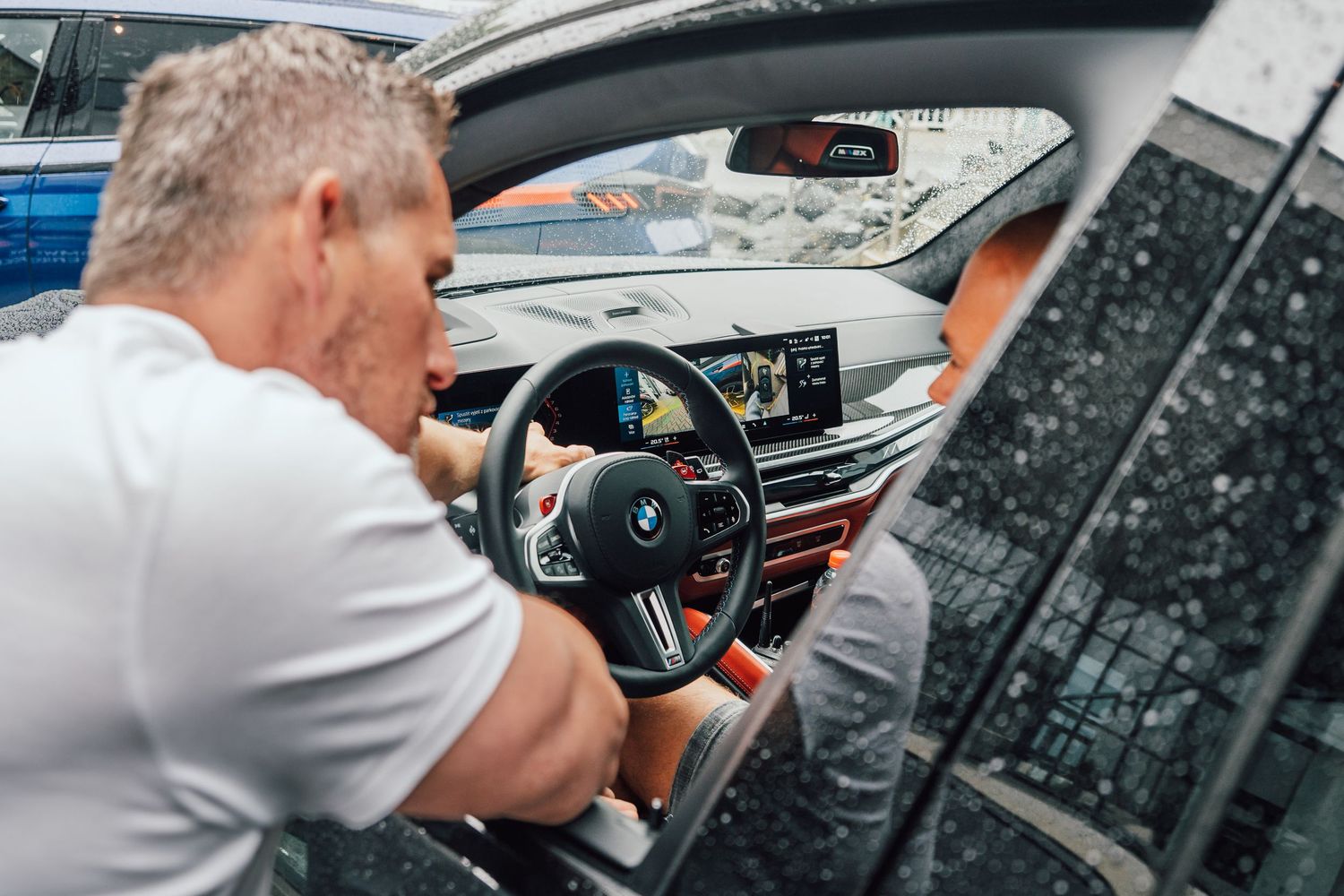 Man examining BMW M car interior featuring M steering wheel and advanced digital cockpit display.