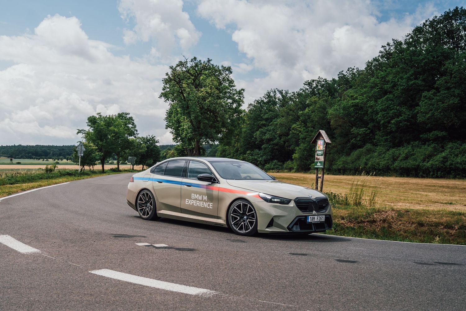 BMW M5 with colorful electric drive livery driving on a rural road surrounded by green trees.