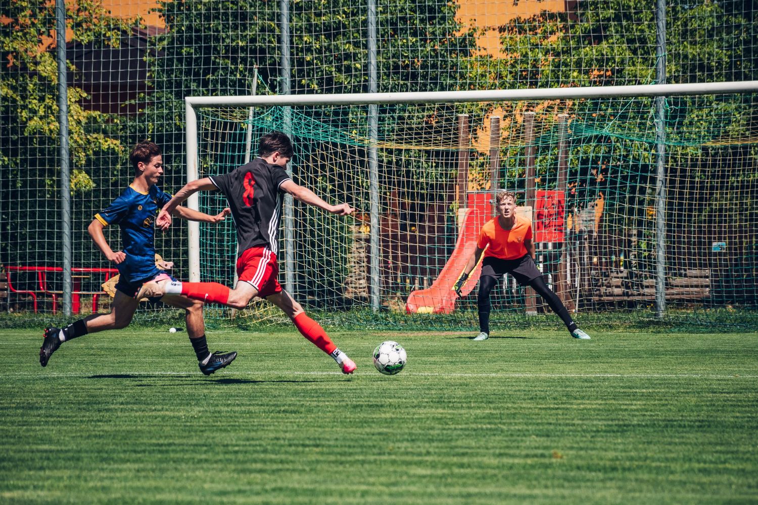 Soccer player attempts a shot on goal as goalkeeper stretches to defend during an outdoor match.