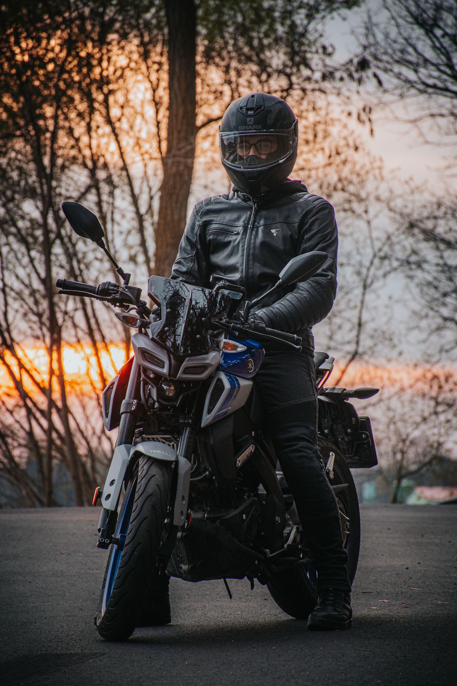 Motorcyclist in black leather gear on sport bike at sunset.