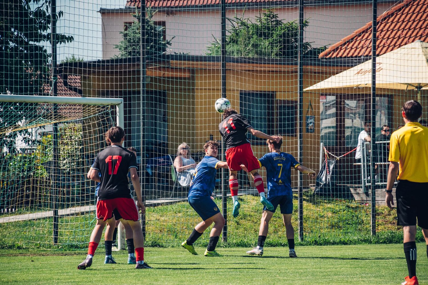 Soccer players jump to contest a header near the goal during a sunny outdoor match.