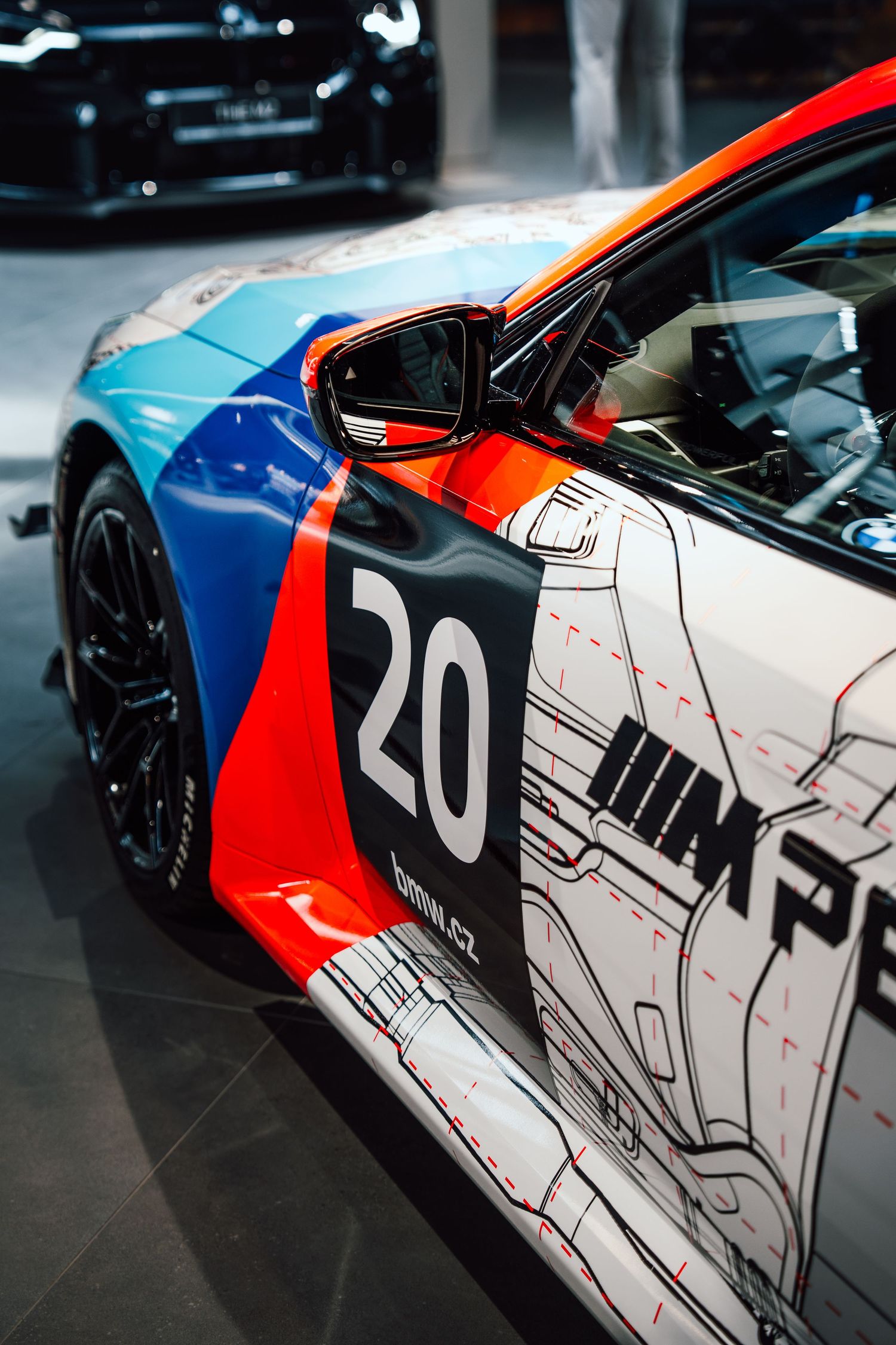 Side view of BMW M2 race car number 20 with vibrant blue, red, and orange M Performance livery.