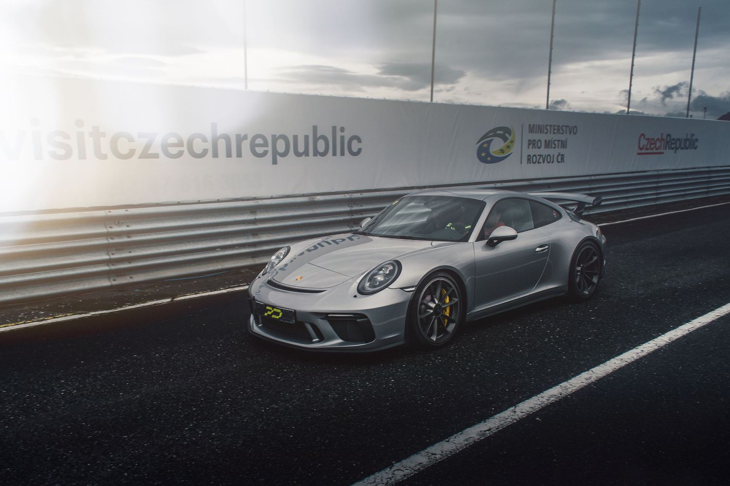 Silver Porsche 911 GT3 on a racing circuit with Visit Czech Republic barrier branding.