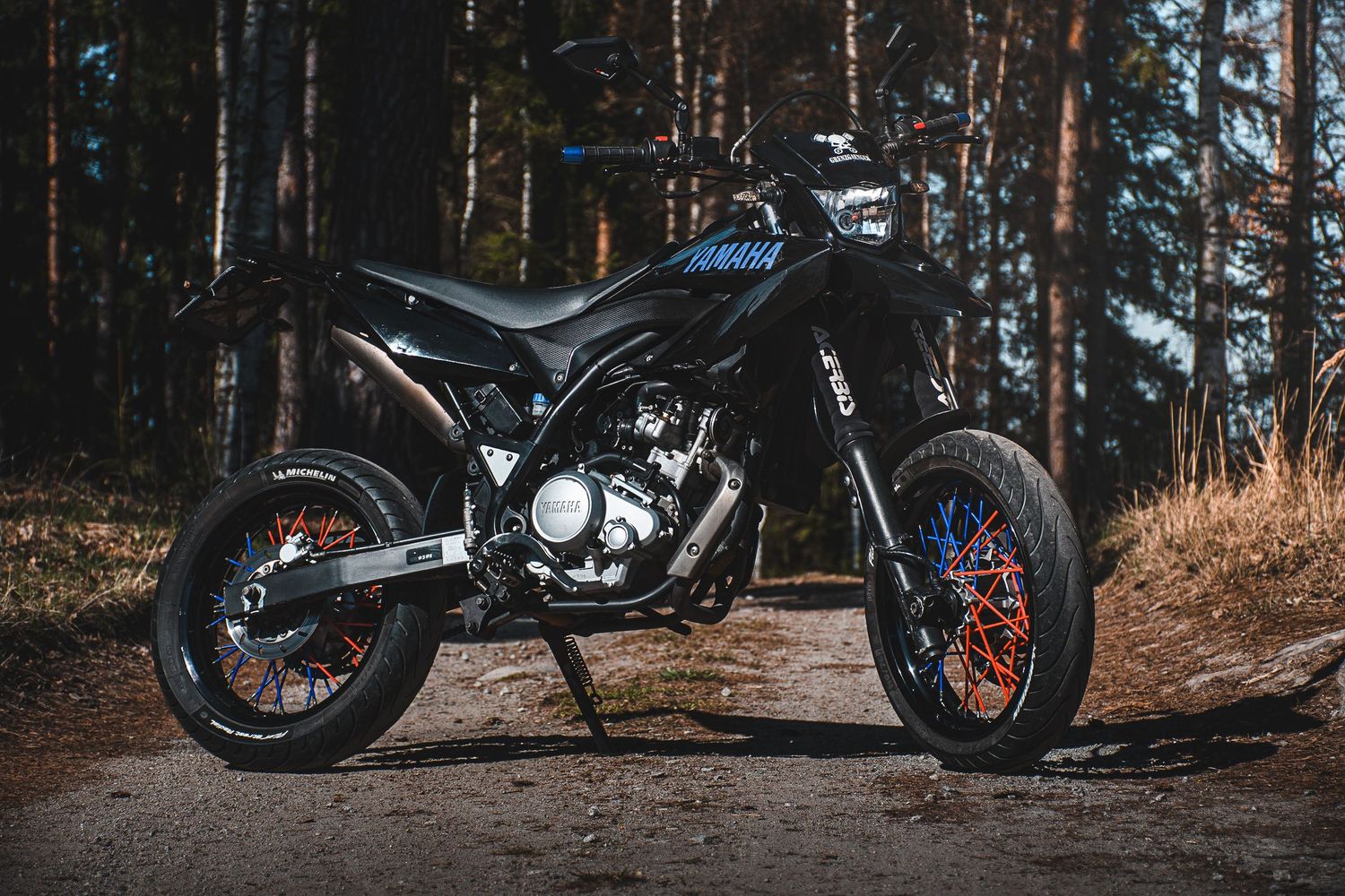 Sleek black Yamaha supermoto motorcycle parked on a dirt path in a pine forest.