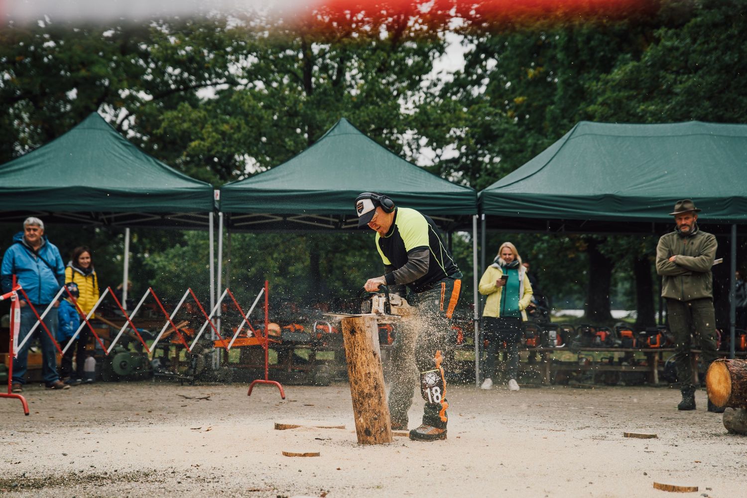 Lumberjack competitor uses chainsaw on large wooden stump at outdoor timber sports competition.