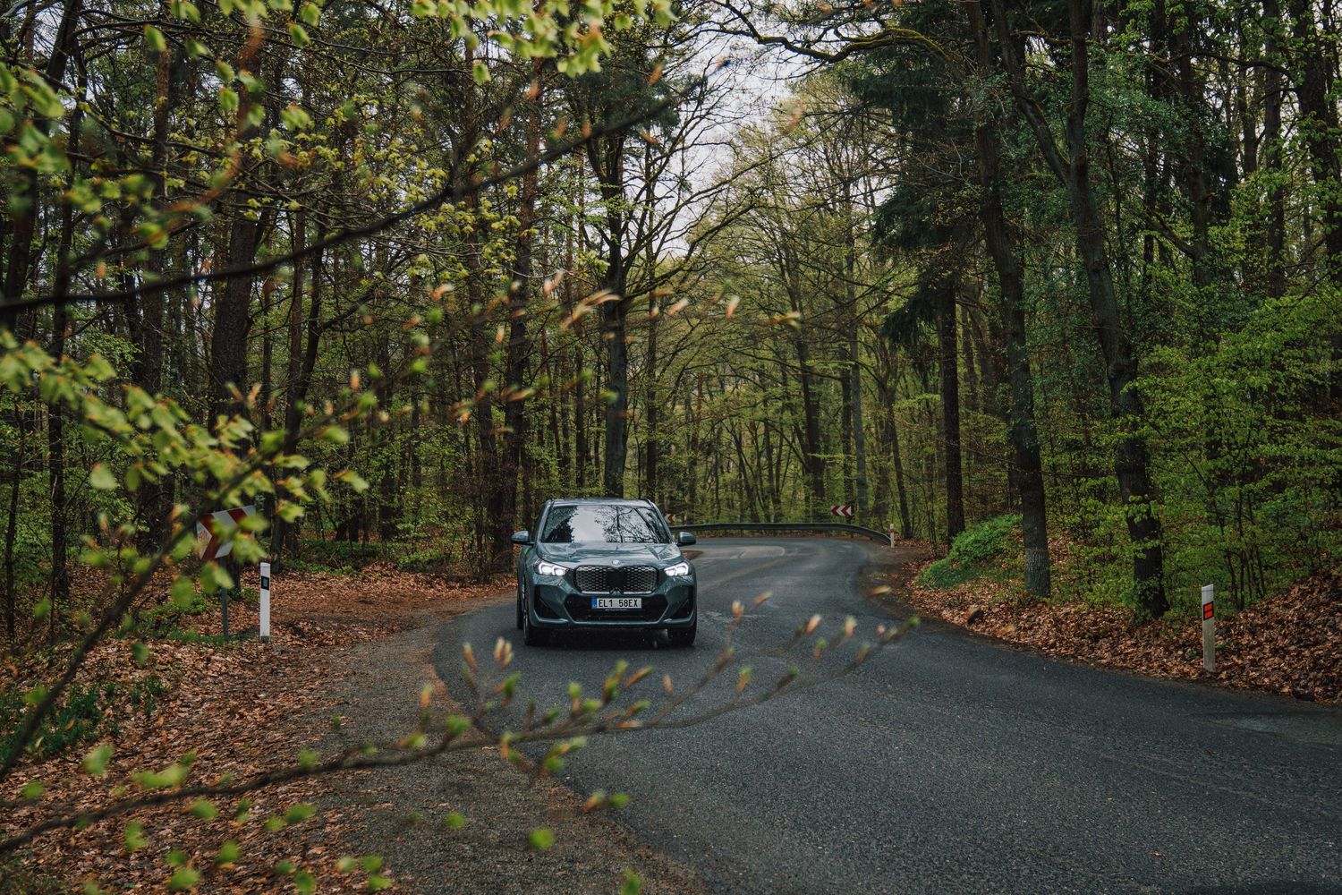 Dark green BMW SUV navigating a winding forest road surrounded by colorful autumn foliage.