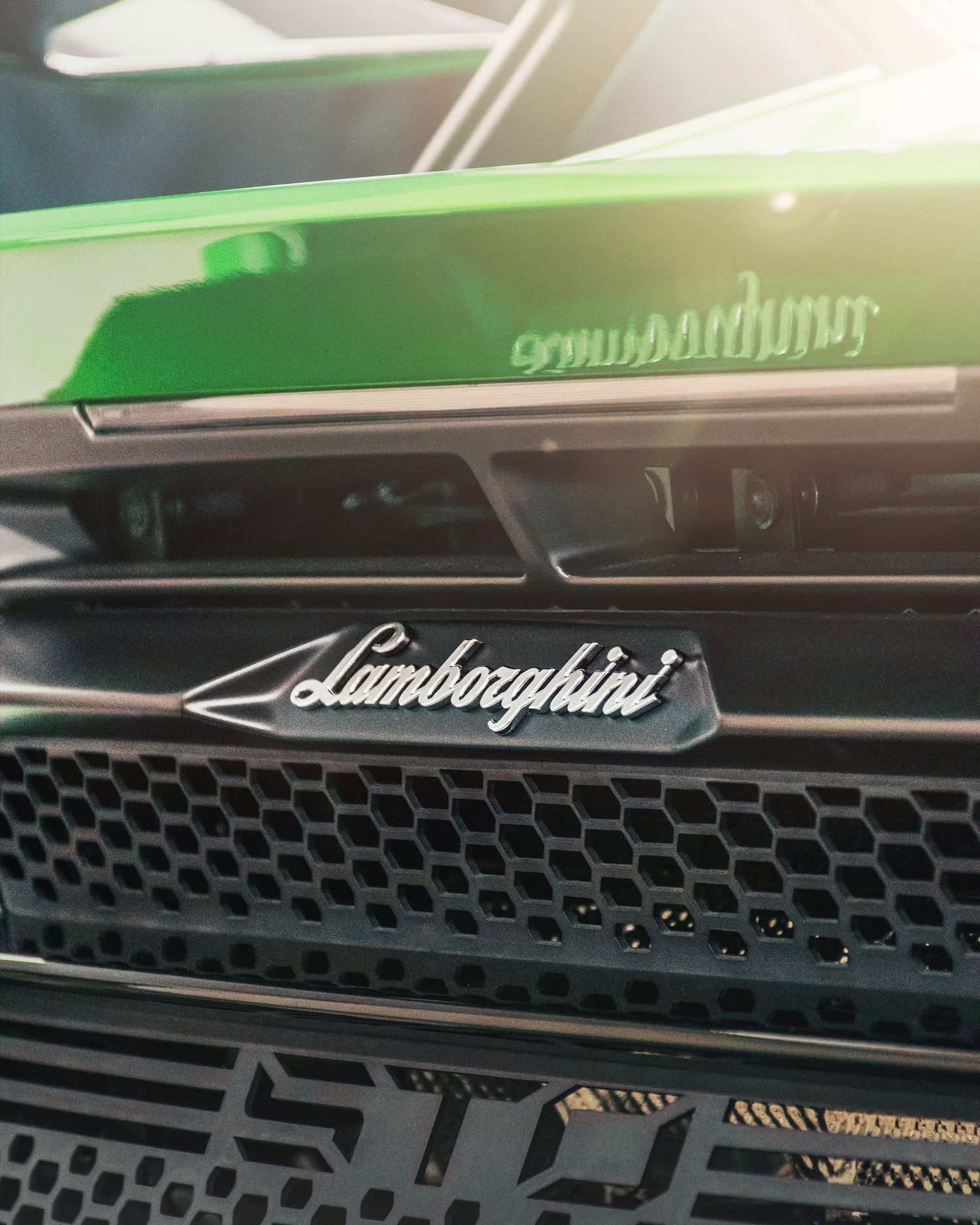 Close-up of a Lamborghini front grille badge on a green supercar in sunlight.