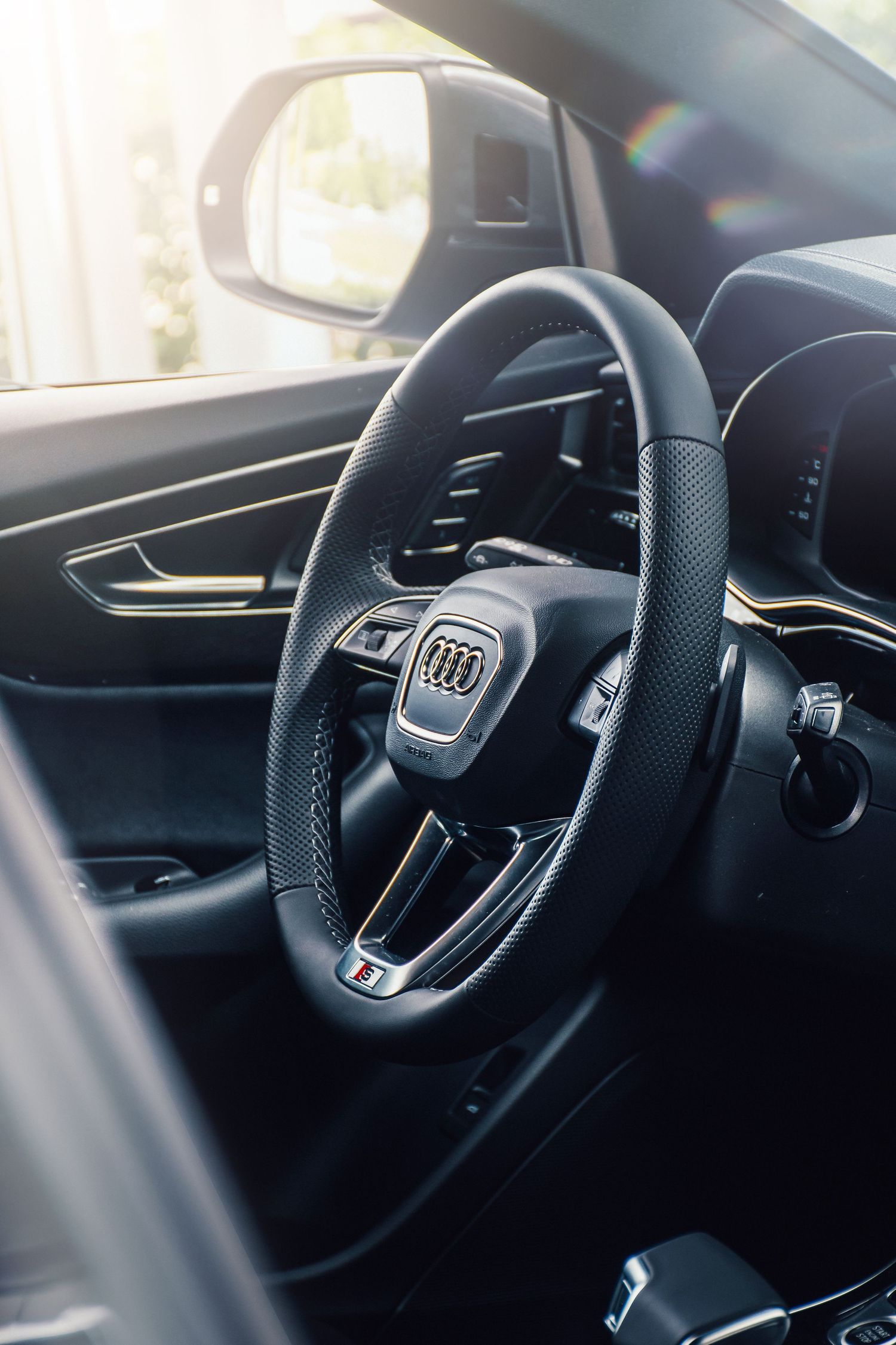Audi S model black leather steering wheel interior shot with sunlight streaming through window in showroom.