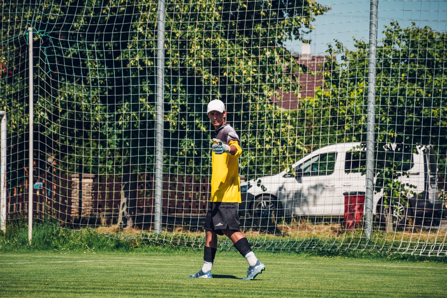 Goalkeeper in yellow jersey stands alert in front of goal net during outdoor soccer match.