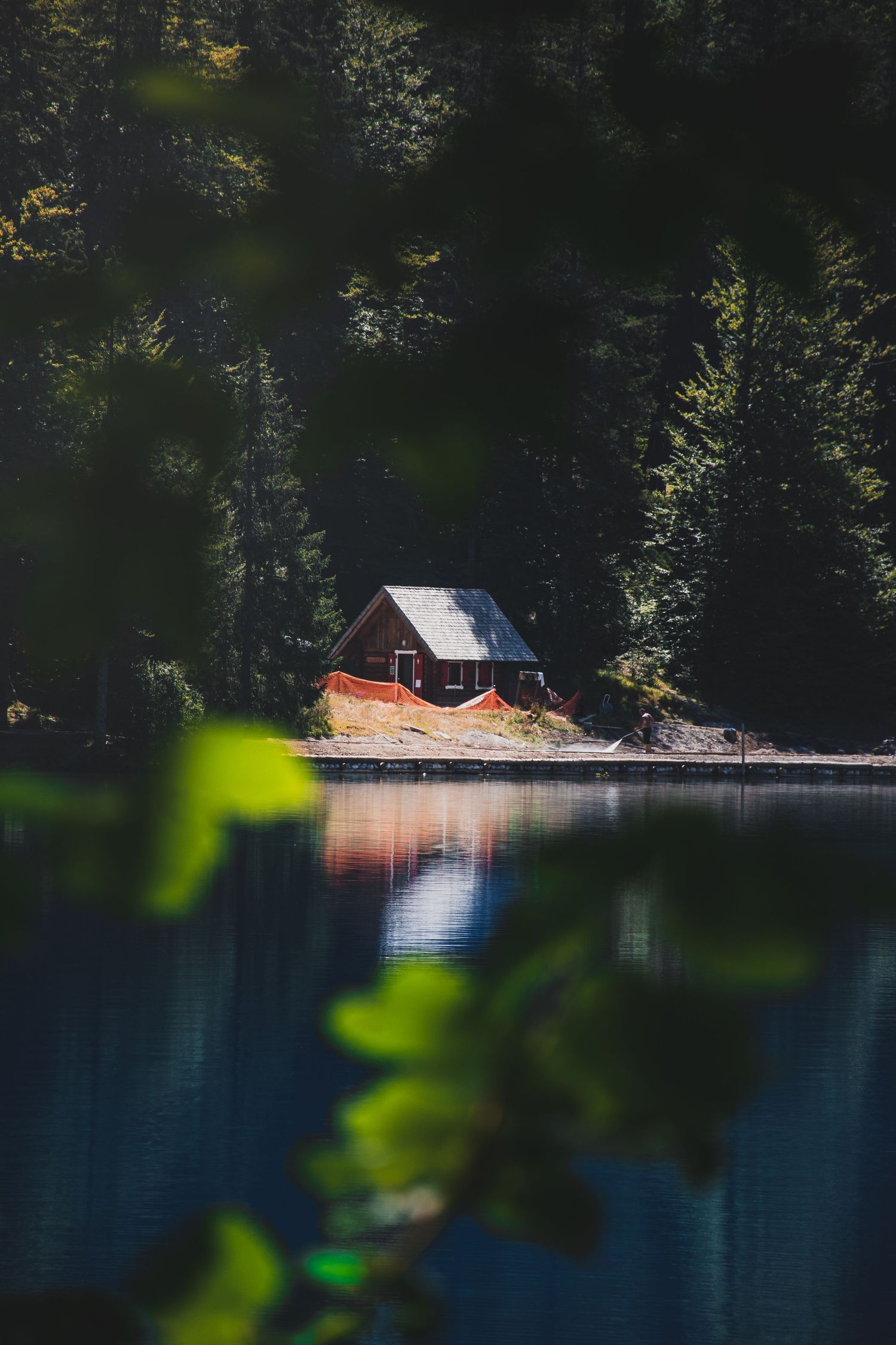 A cozy wooden cabin nestled among dense evergreen trees reflected in a calm, still forest lake.