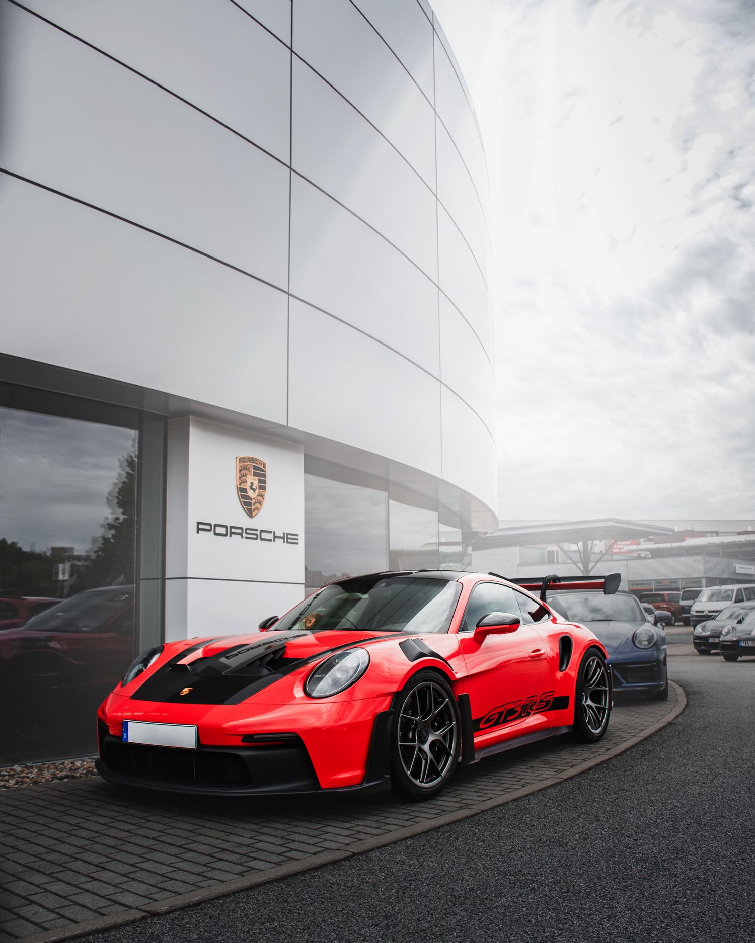 Red Porsche 911 GT3 RS sports car parked outside an official Porsche dealership building.