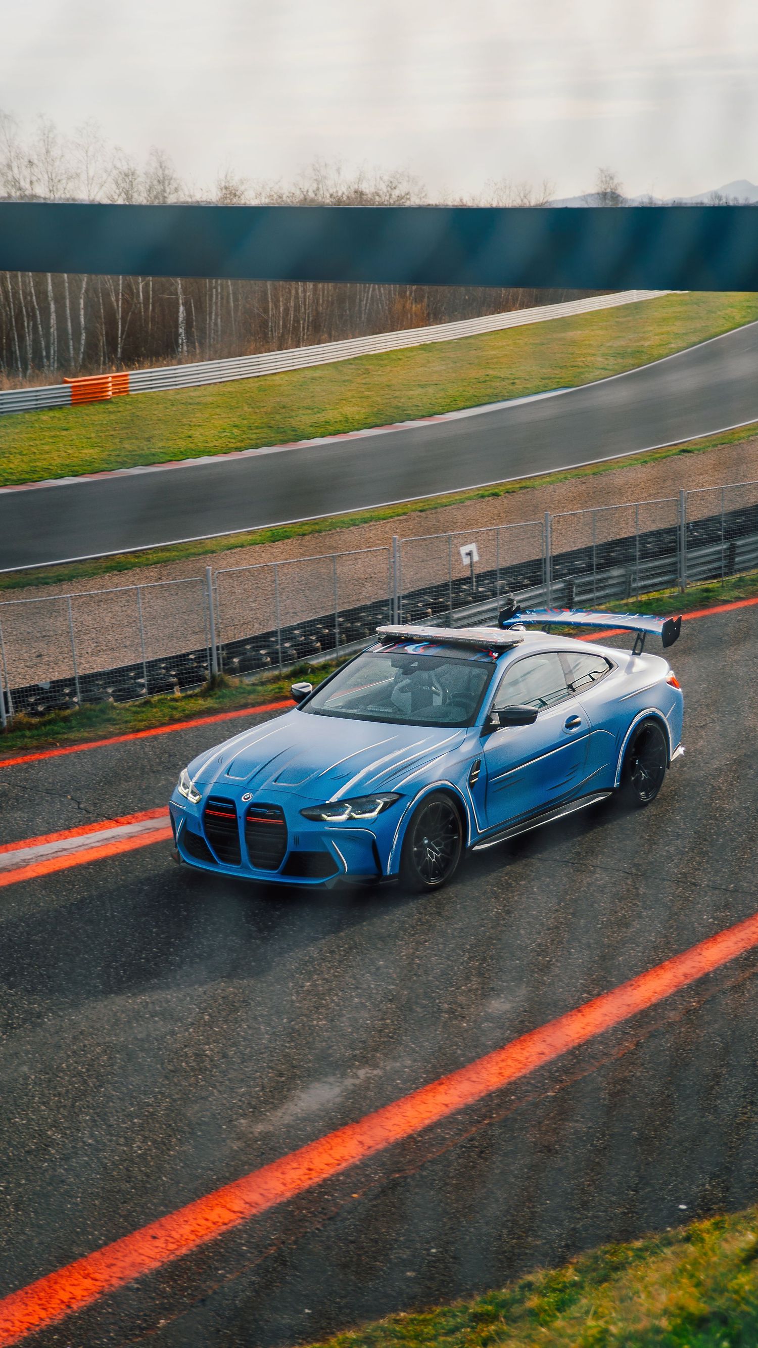 Blue BMW M4 GT3 race car on a wet racing circuit track with large rear spoiler.