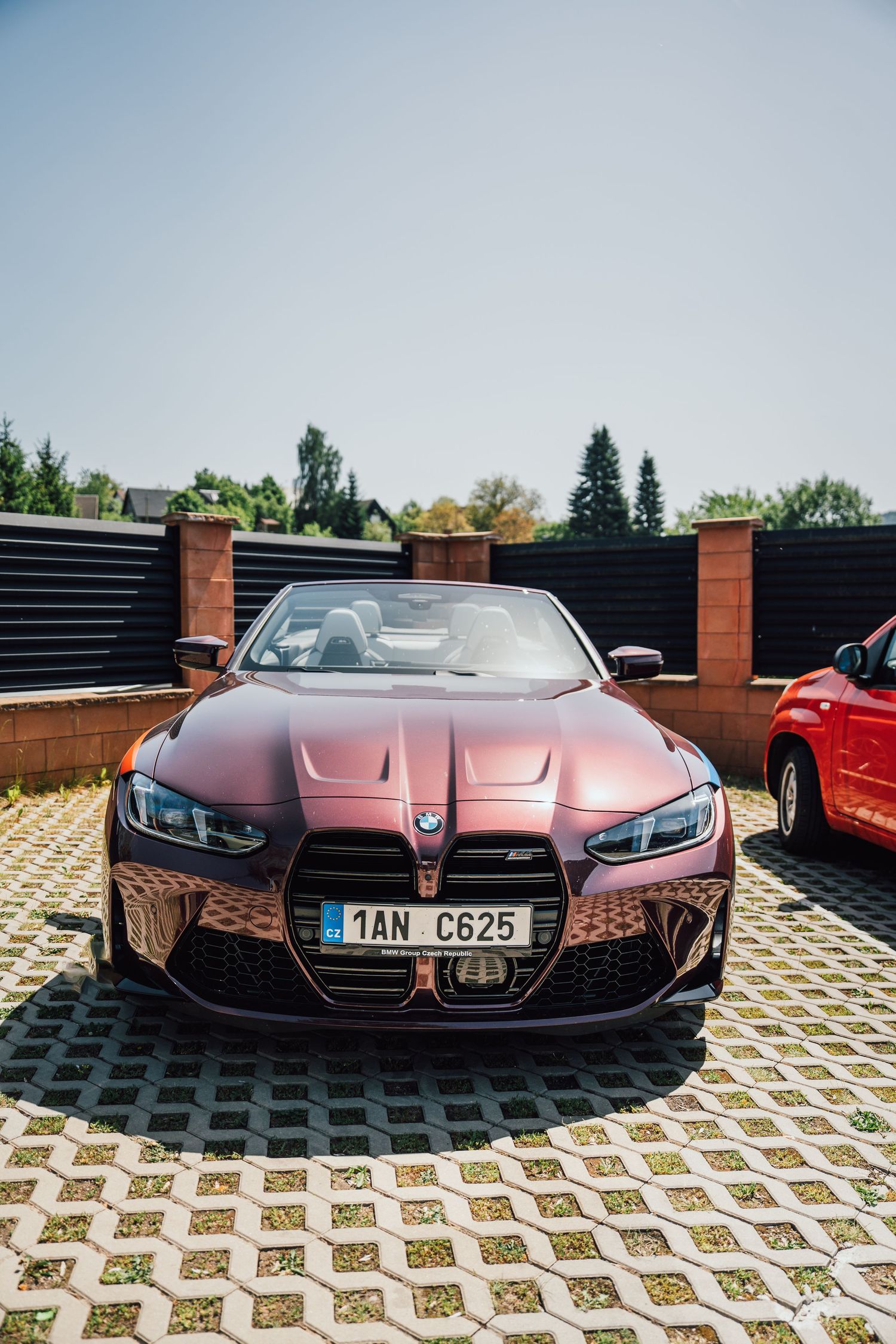 Front view of a dark red BMW M4 convertible with Czech license plate parked on cobblestones.