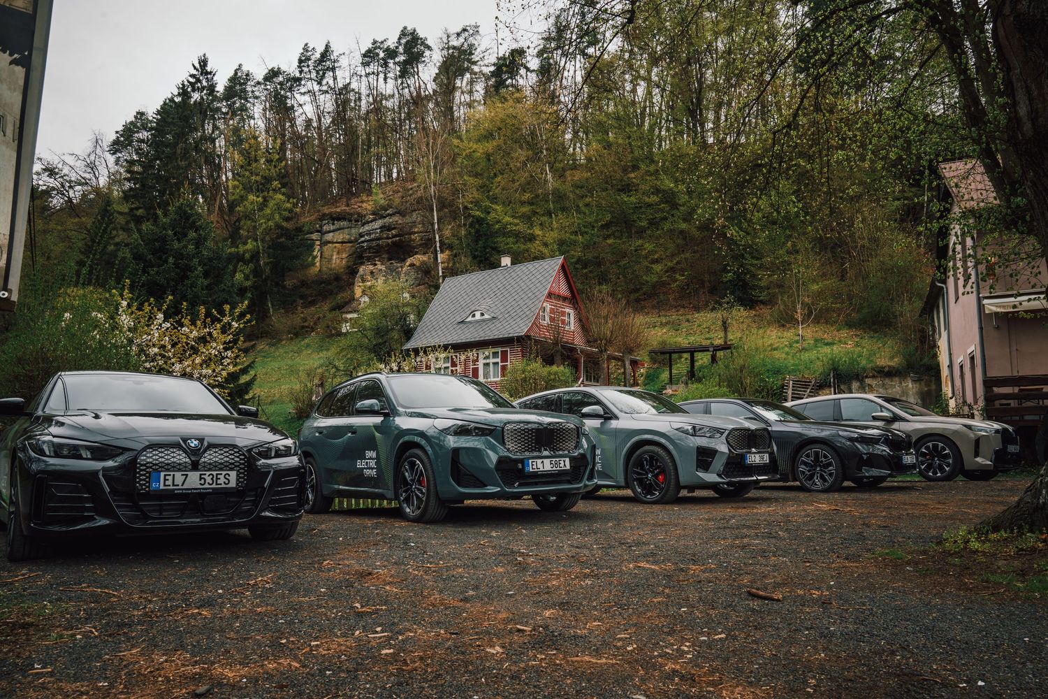 Four luxury electric SUVs including Audi models parked on gravel in front of a forest cottage in autumn.