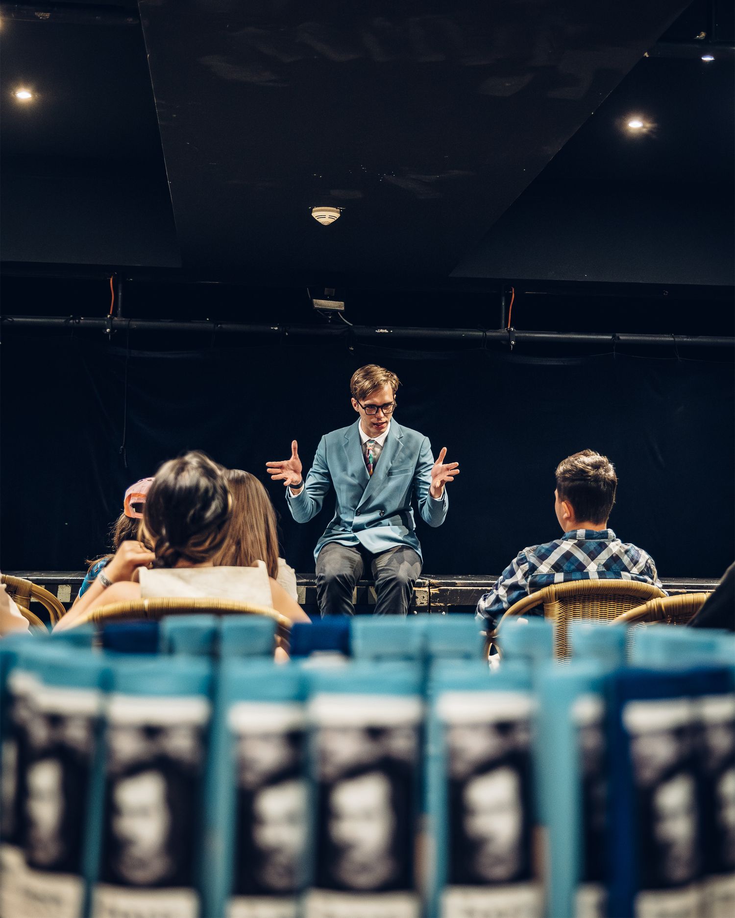 Man in blue suit speaks to seated audience in a small theater setting.
